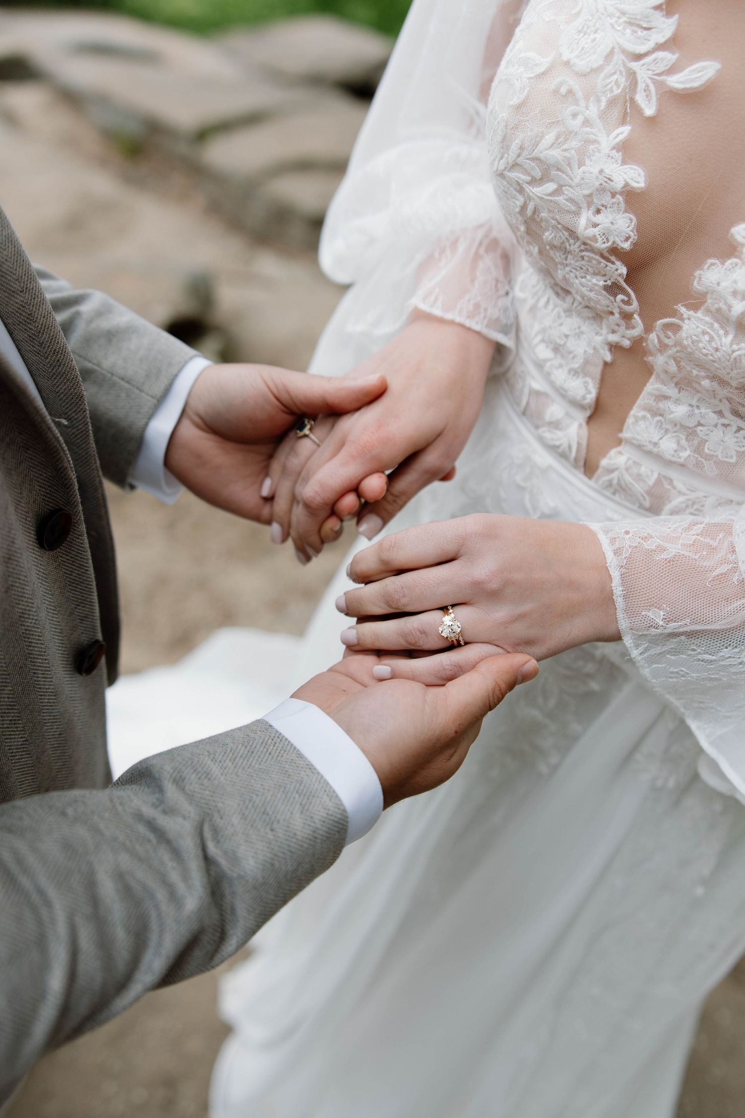Close-up of wedding couple holding hands, showing white lace dress sleeve, gray suit sleeve and engagement ring.