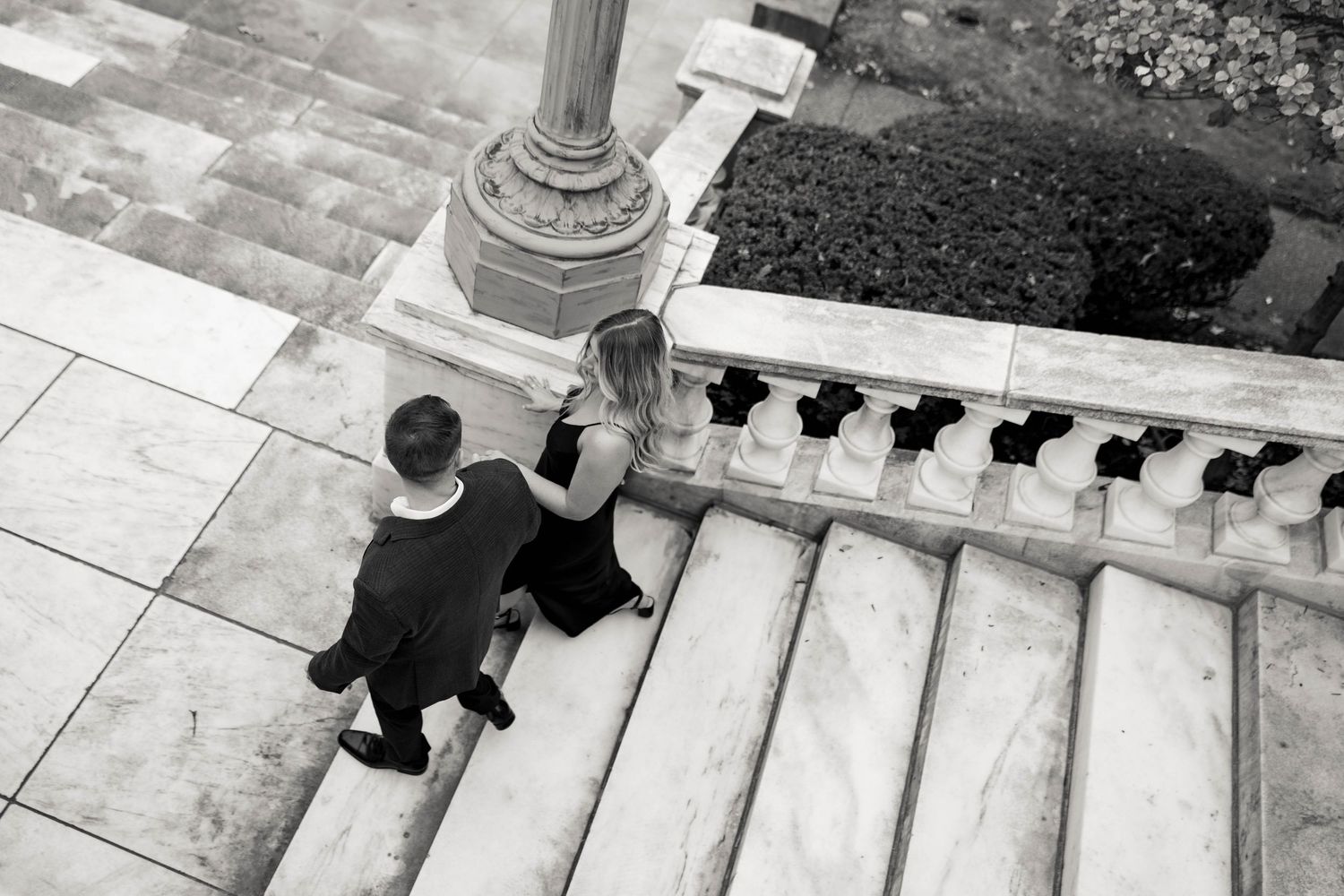 A black and white overhead view of a couple ascending a grand stone staircase with decorative columns and railings. Cleveland, OH