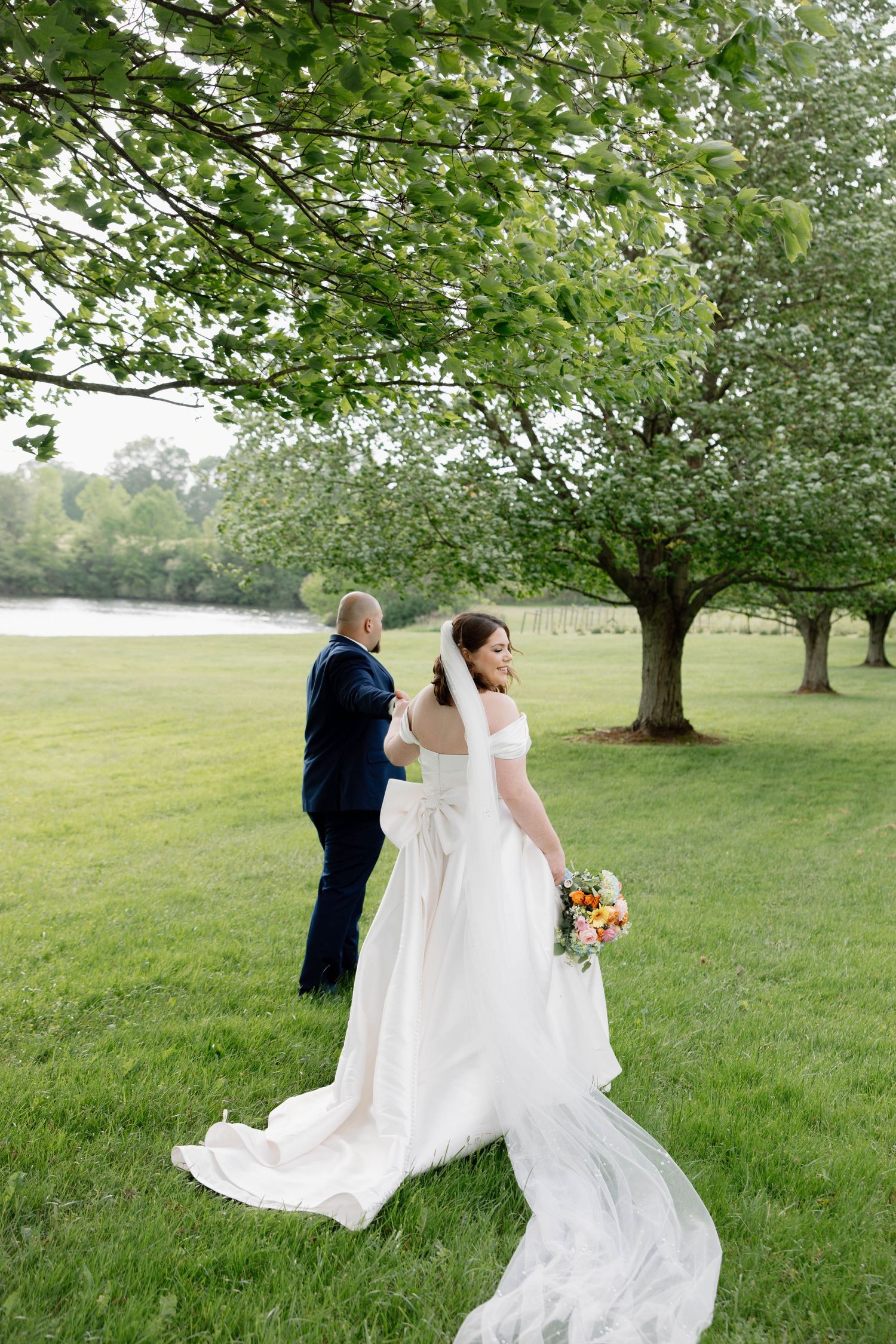 A couple sharing a romantic moment under trees on their wedding day with a flowing white dress and bouquet.