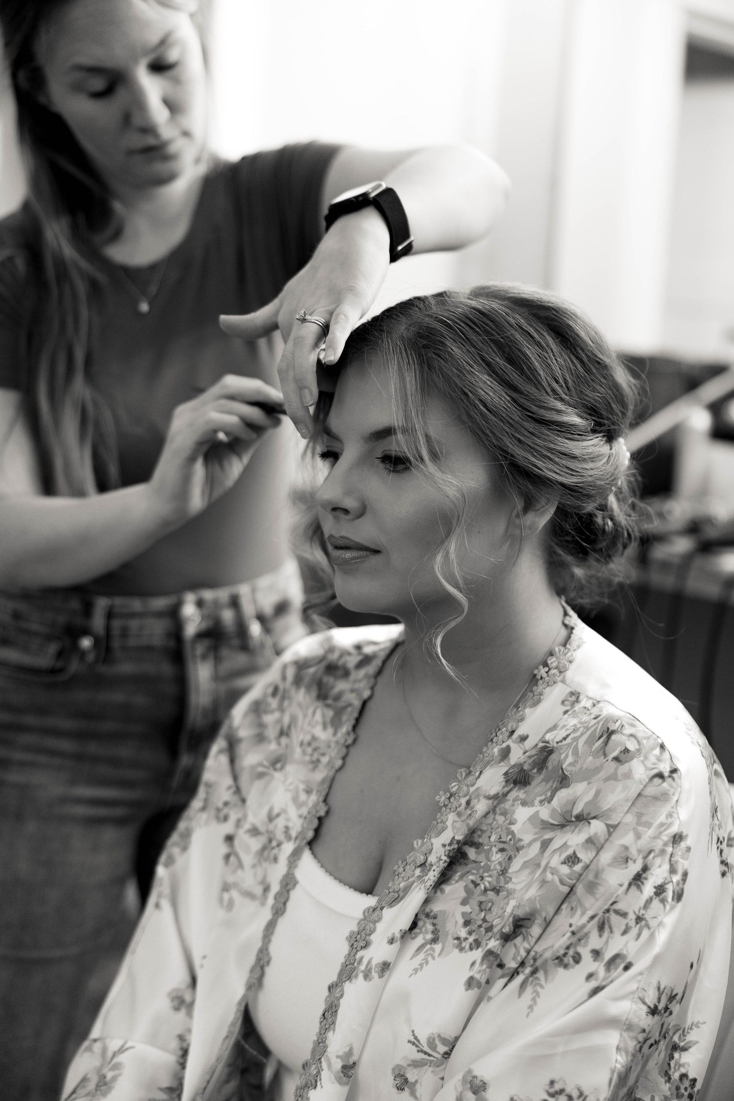 A woman gets her hair styled in black and white photography while wearing a floral robe.
