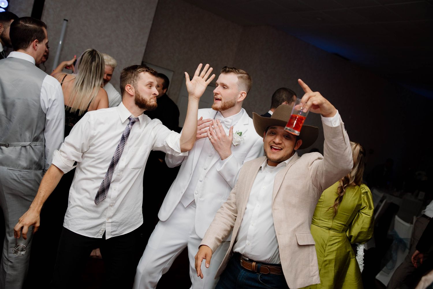 Group of people dancing and celebrating energetically at a party with people wearing white shirts and formal attire.