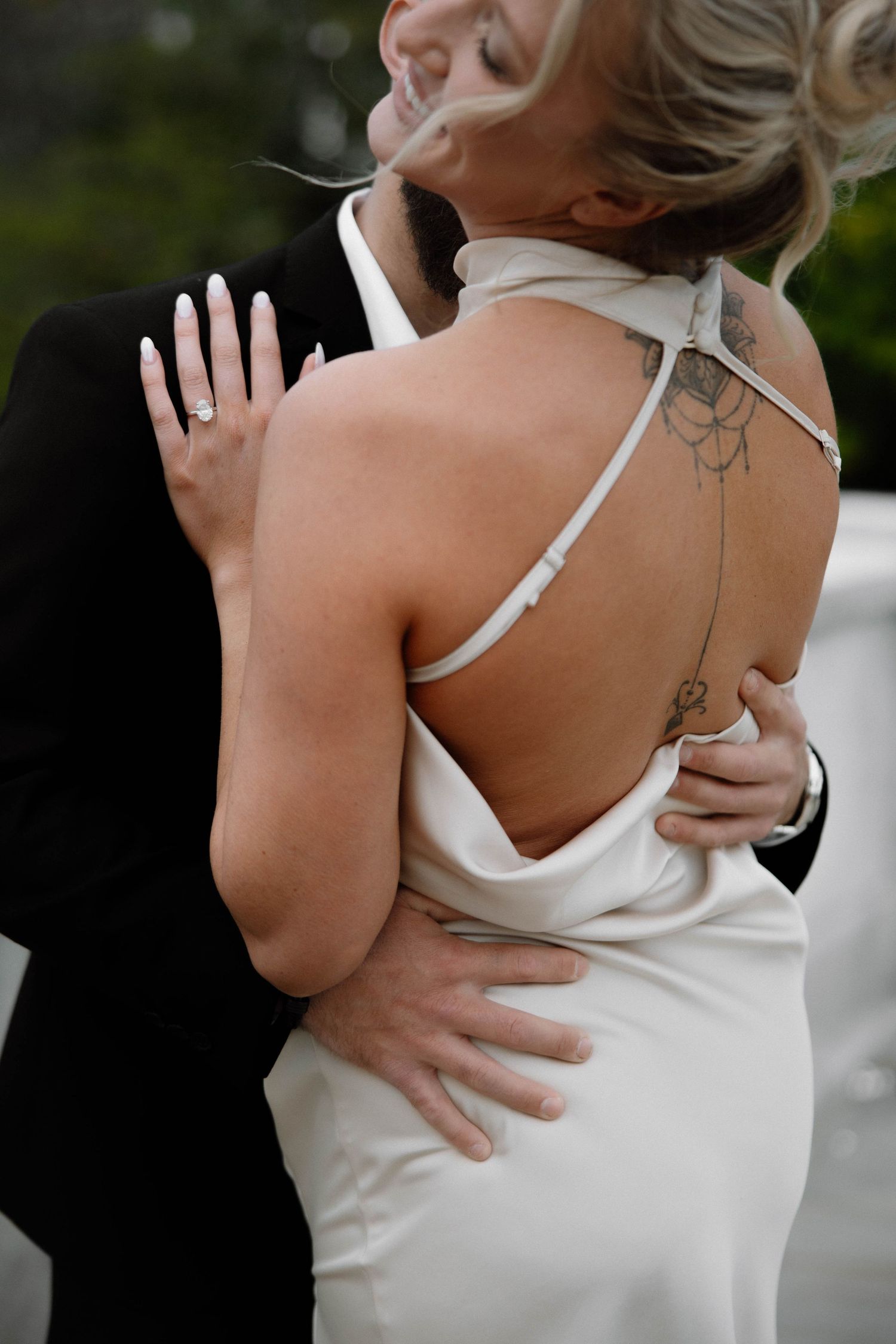 Close-up of newlyweds embracing, showing white wedding dress with open back. Cleveland, OH