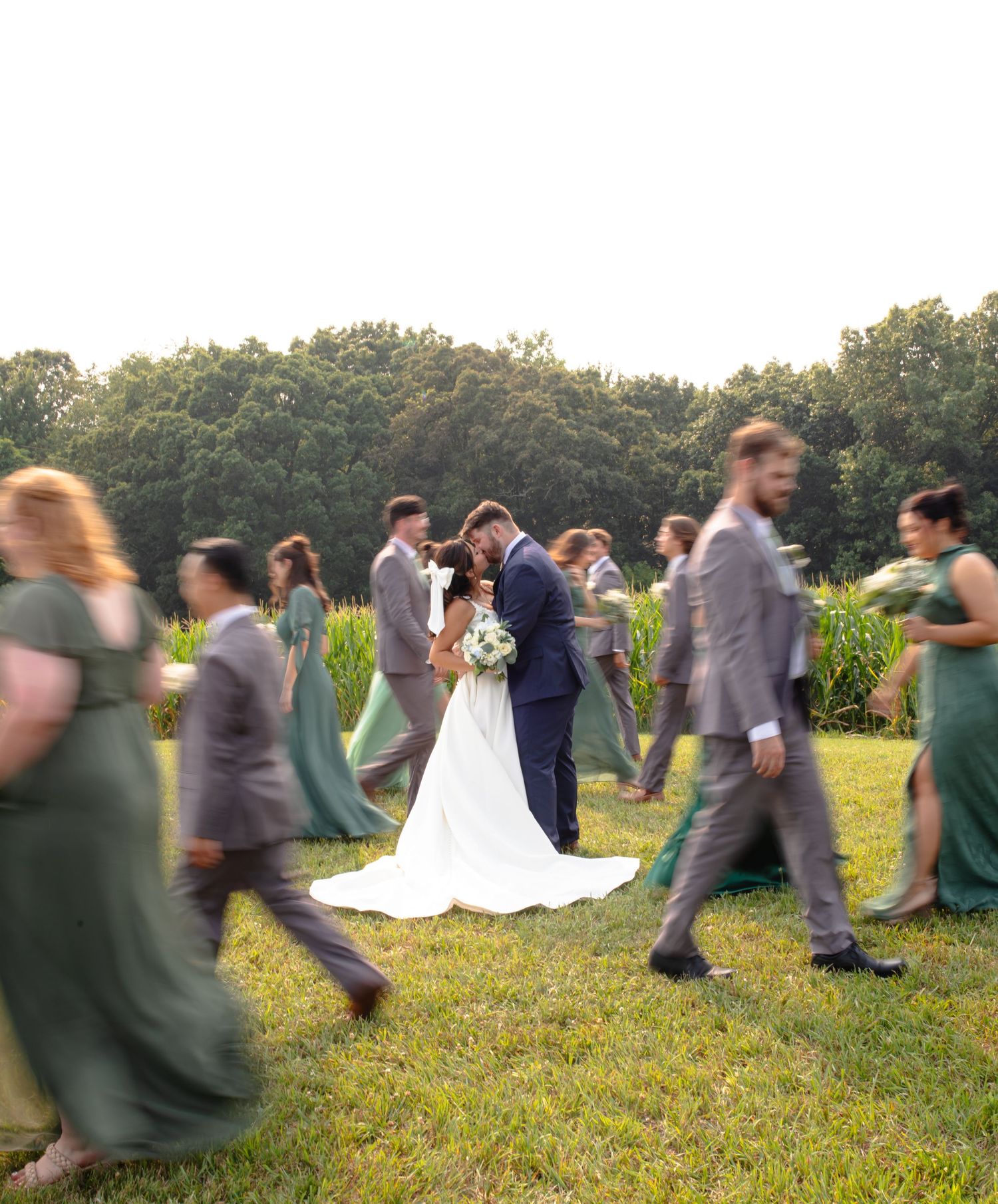 Motion-blurred sequence of wedding guests circling newlyweds in a sunny outdoor garden ceremony setting at sunset.