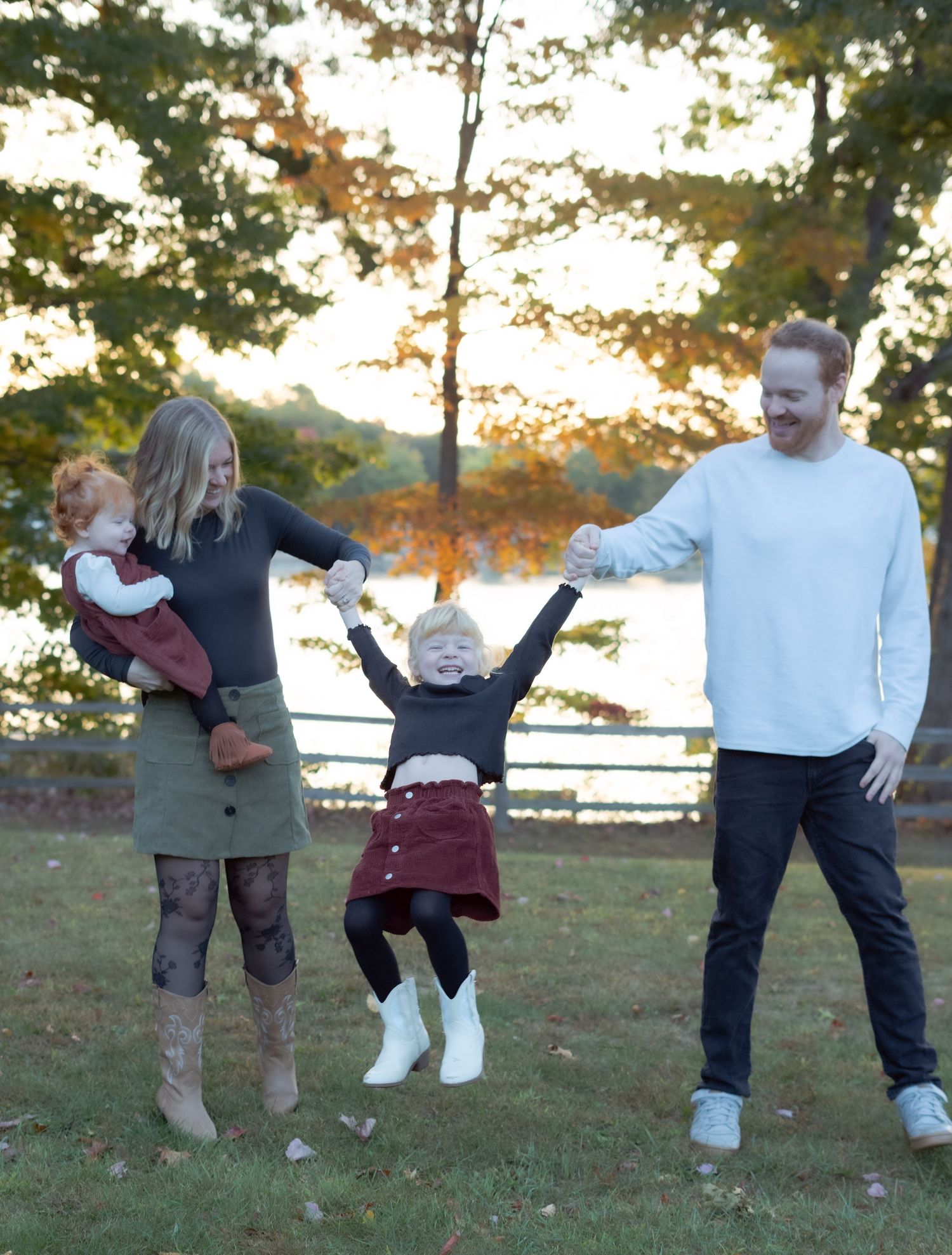 A playful outdoor family photo with a child being lifted up while everyone smiles at sunset.