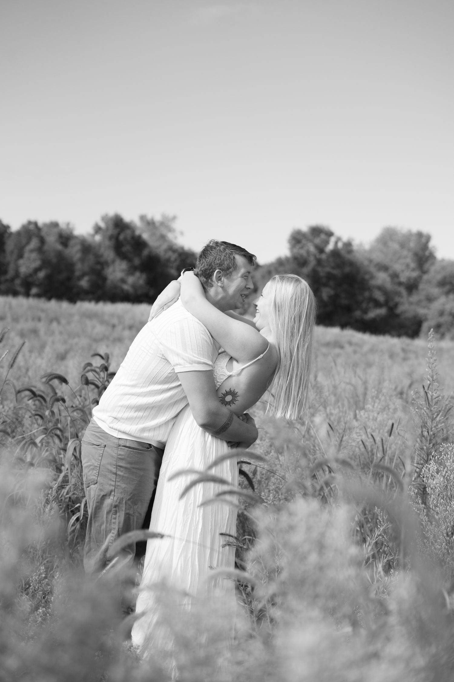A romantic black and white photo sequence shows a couple embracing in a tall grass field during a sunny day.