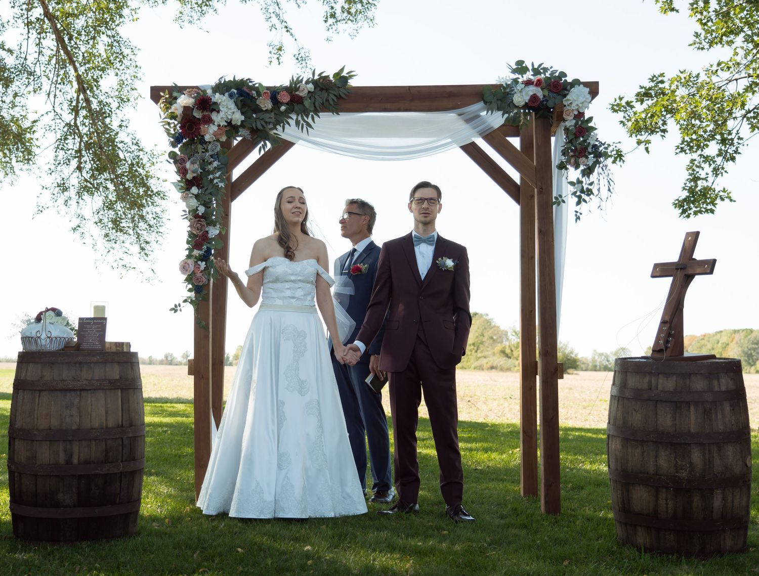 Wedding ceremony under wooden arch with wine barrels and rustic decor.