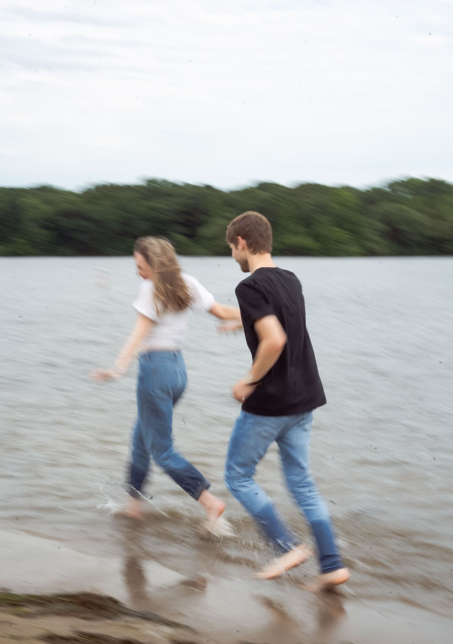 Couple running playfully through shallow water at the beach's edge in a candid moment.
