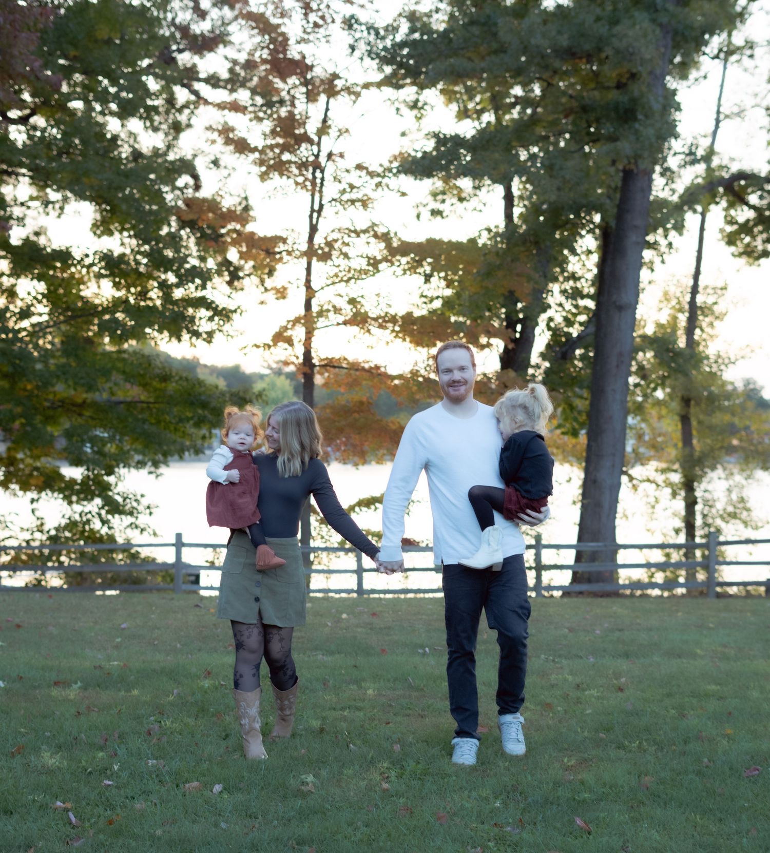 A family walking together outdoors with a sunset and fence in the background.