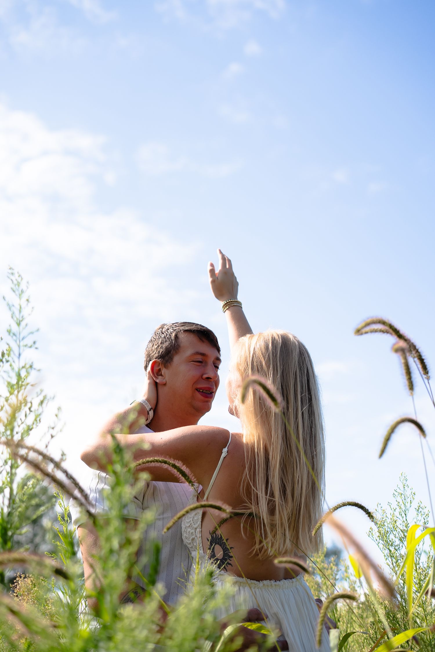 A couple shares a romantic moment together in a sunlit field of tall grass and wildflowers.