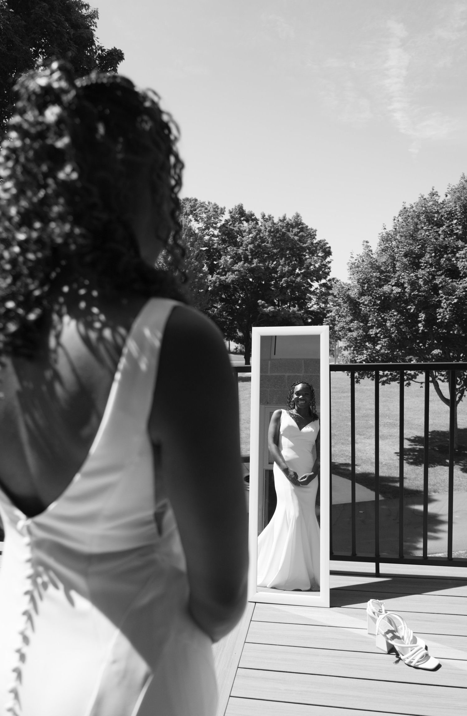 A black and white wedding photo showing a bride in white dress reflected in mirror on outdoor wooden deck.
