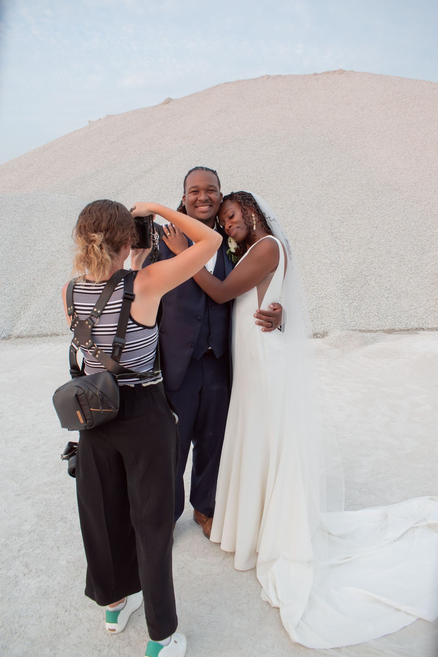 A wedding photographer documents a candid moment against white stone walls.