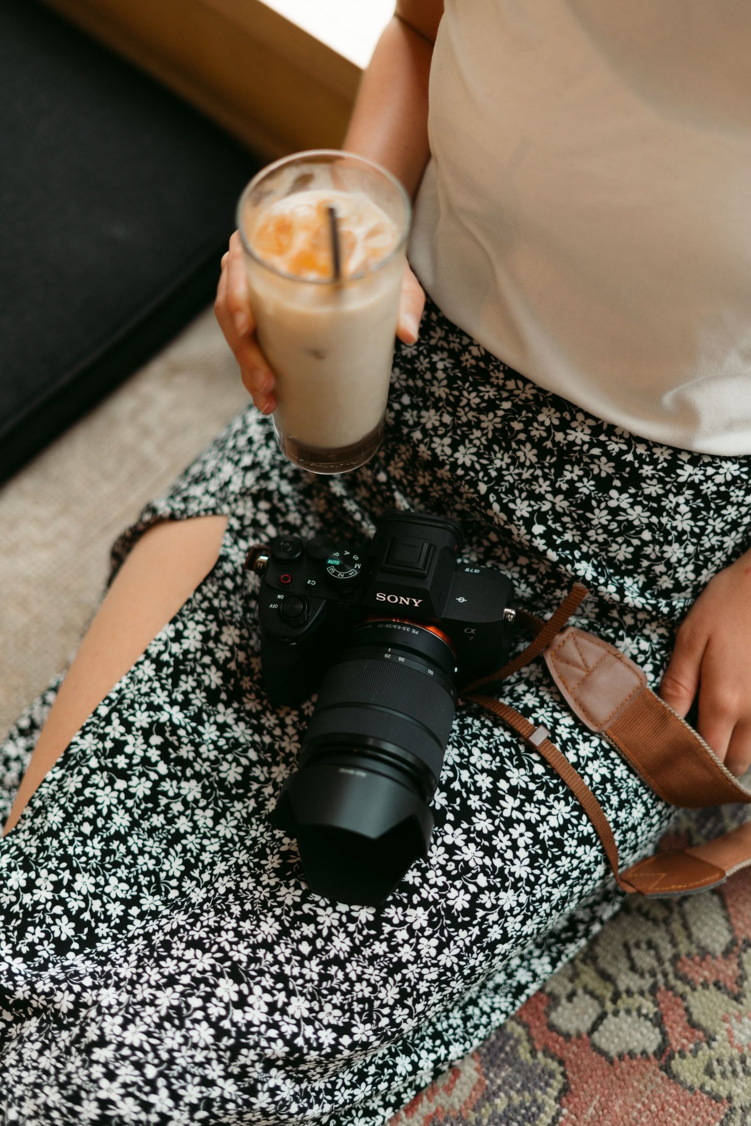 Sony camera and iced coffee drink resting on a floral patterned fabric.