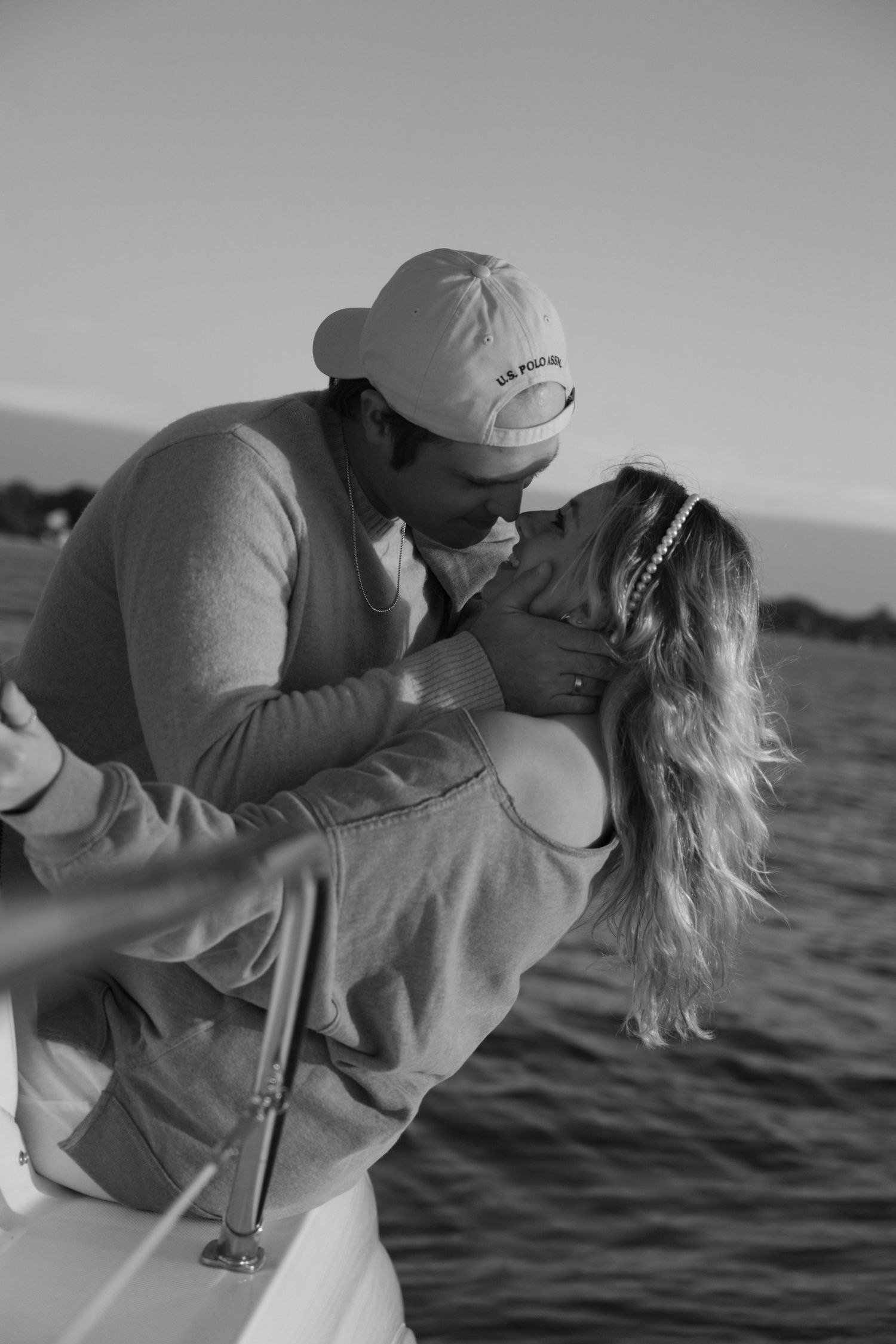 A romantic black and white photo of a couple embracing on a boat with water in the background.