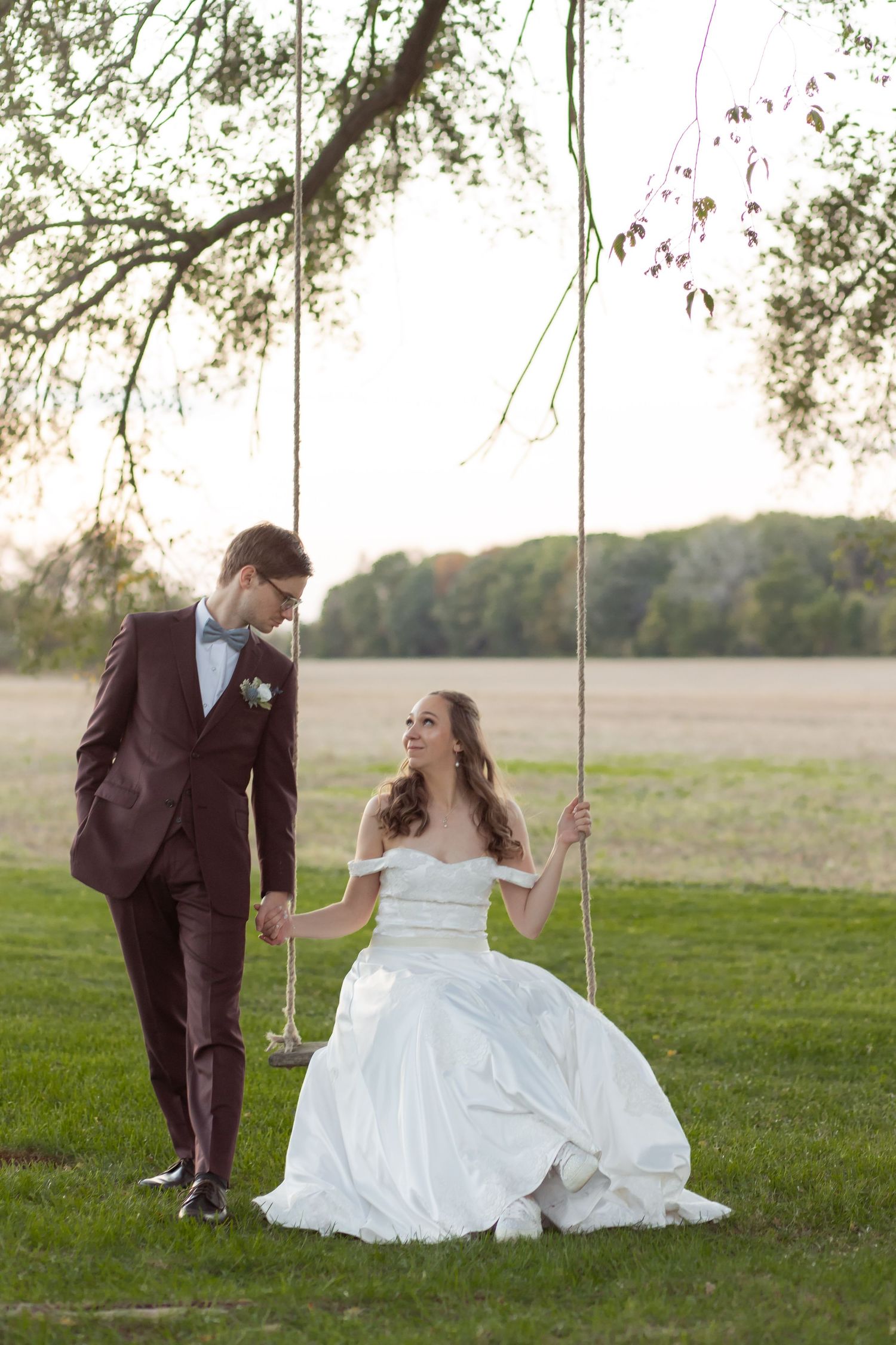 A couple sharing a sweet moment on a tree swing in wedding attire during their countryside celebration.
