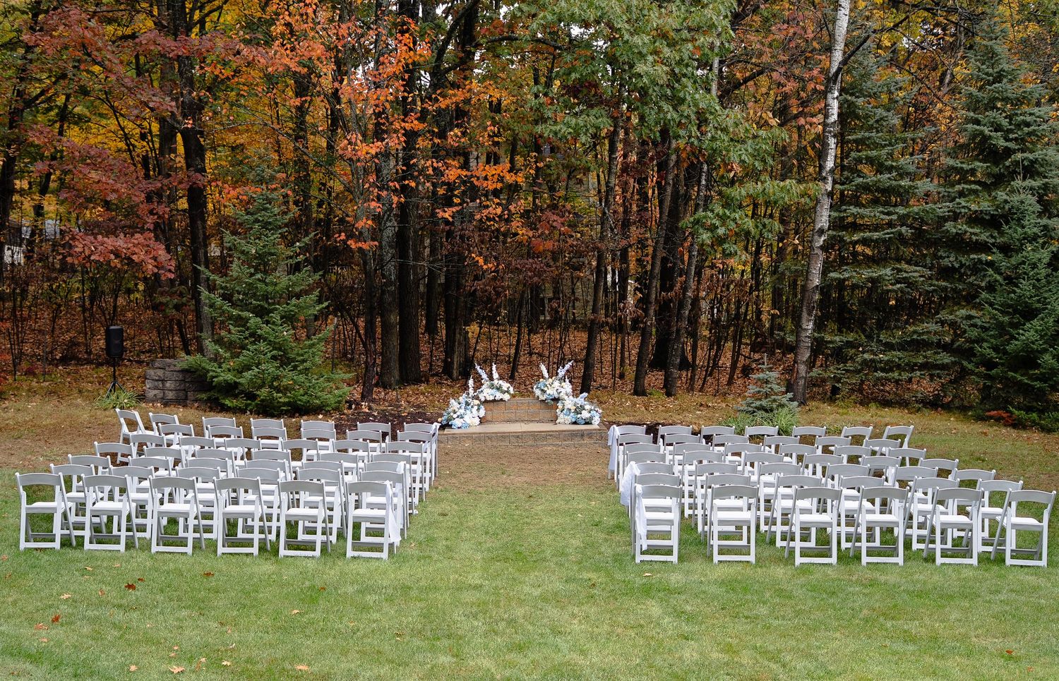 White chairs arranged in rows for an outdoor wedding ceremony with vibrant autumn foliage in the background.