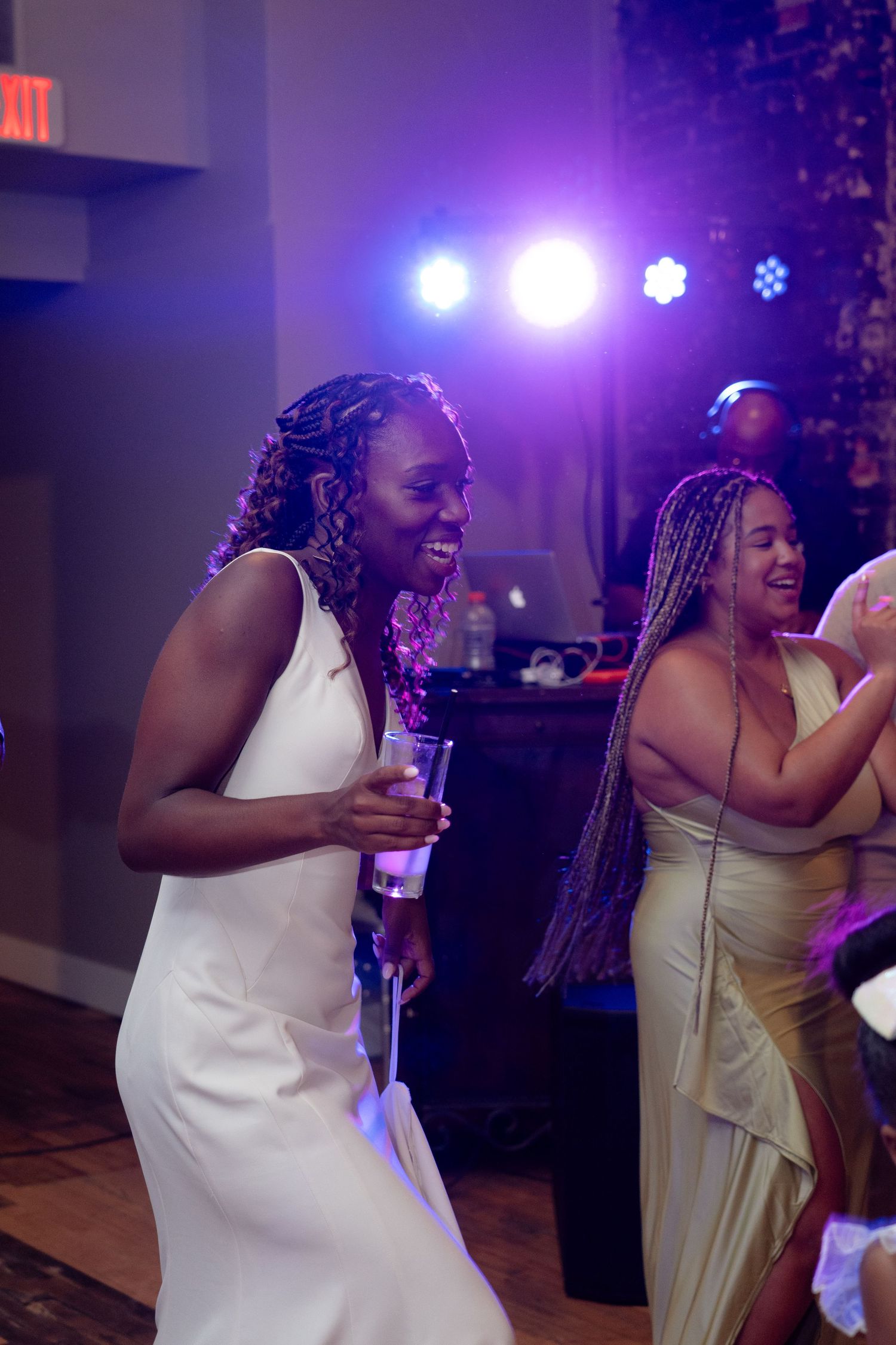 Guests dancing and celebrating at a wedding reception with purple stage lighting in the background.