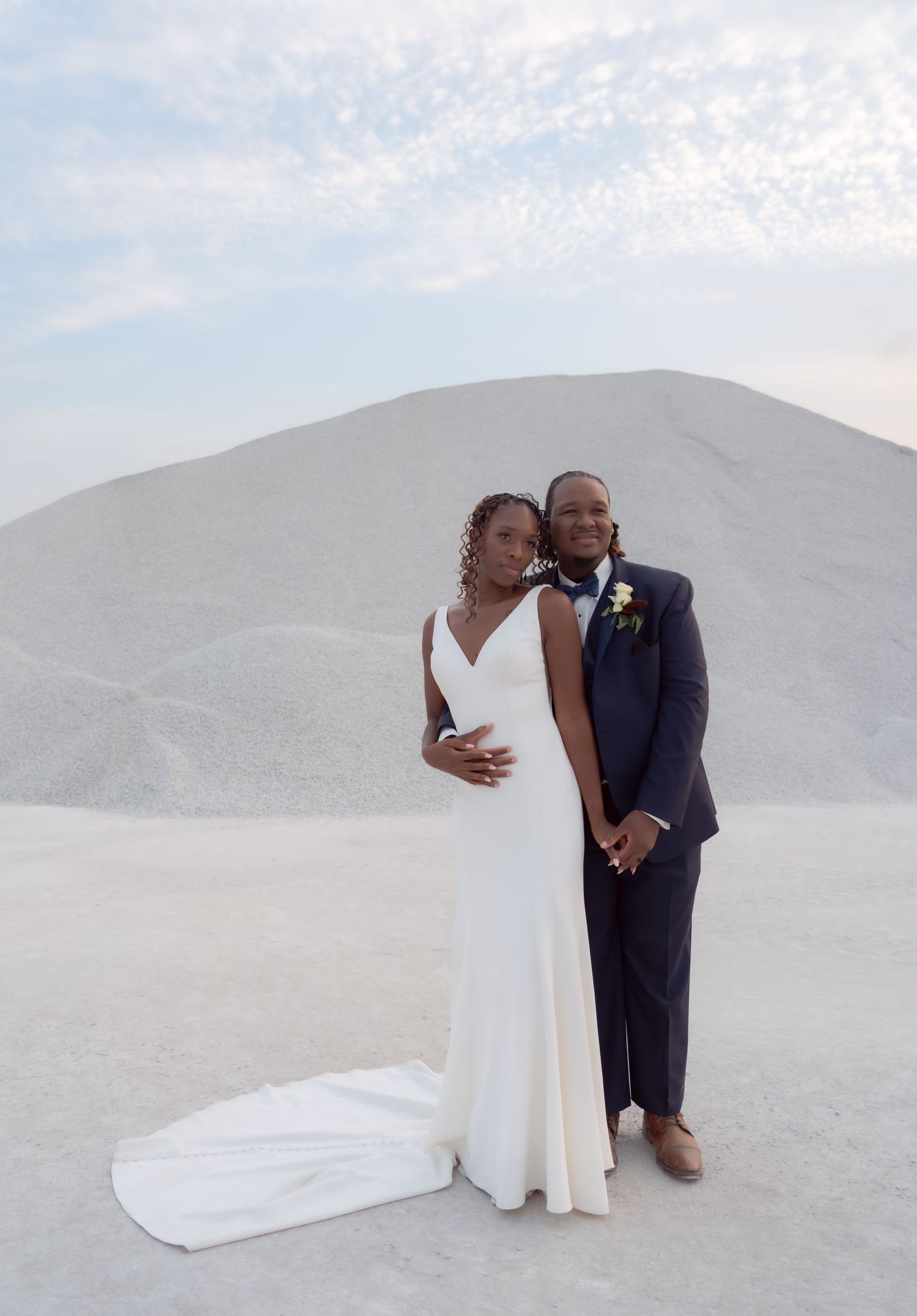 A happy newlywed couple poses together against white sand dunes on their wedding day.