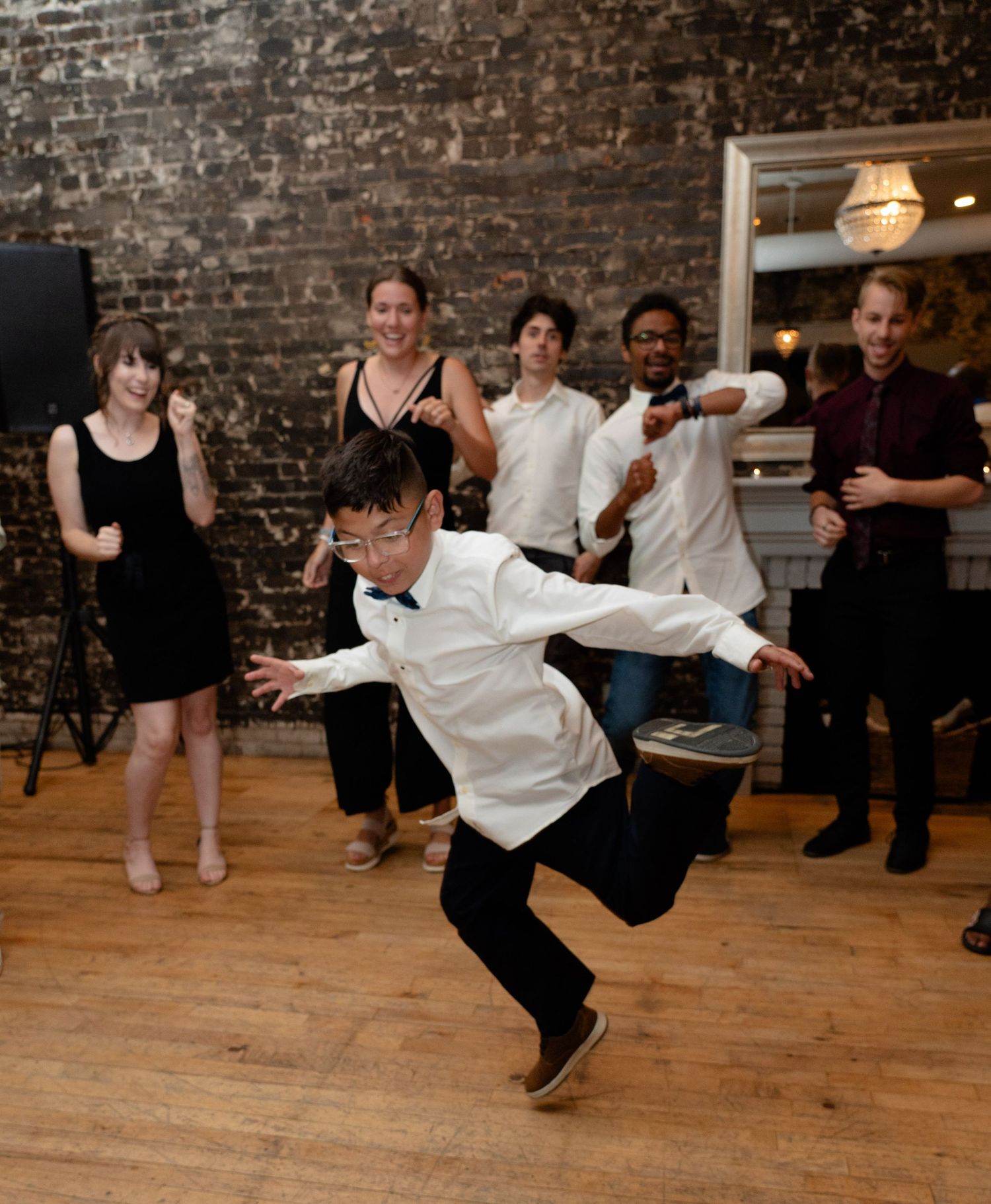 Dancers celebrate on a wooden dance floor in front of an exposed brick wall at a party gathering.