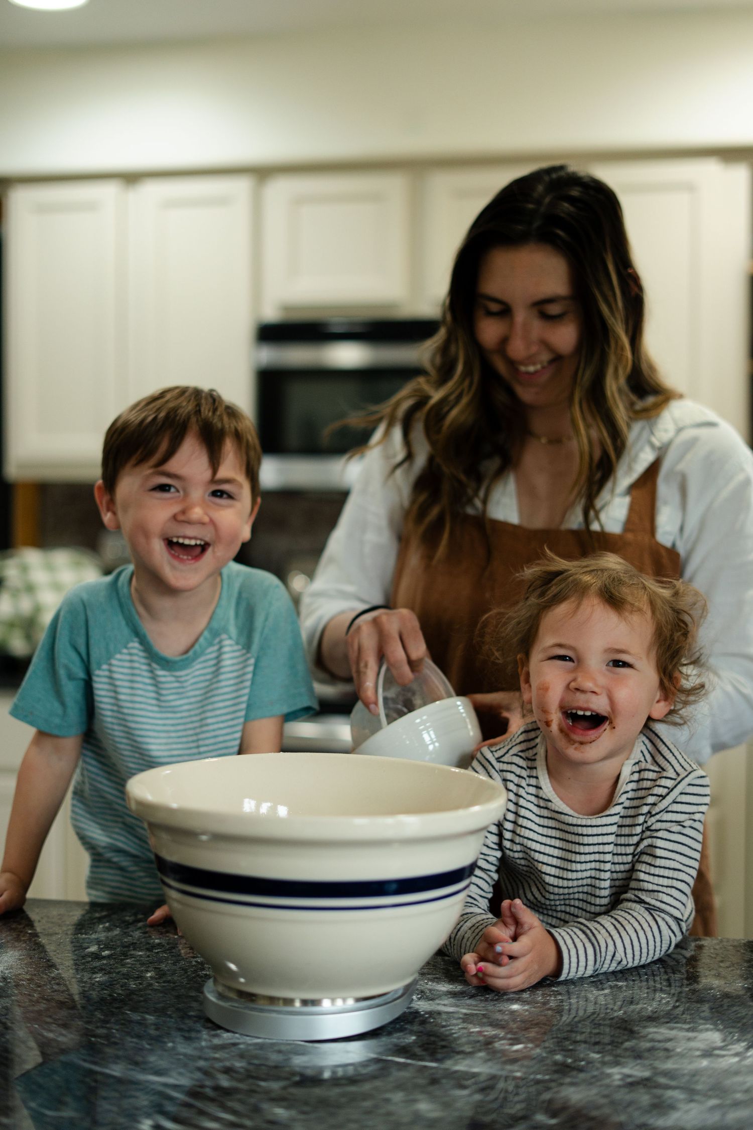 A joyful moment in the kitchen as a family laughs while baking together with a large mixing bowl on the counter.