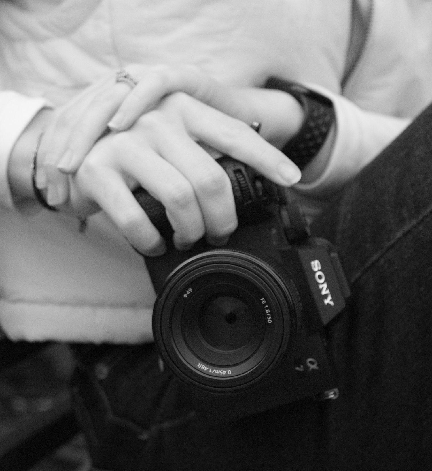 Close-up black and white shot of hands holding a Sony camera lens.