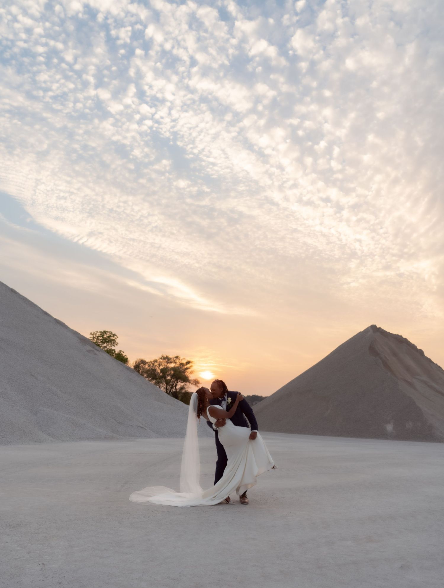 Wedding couple embraces during sunset among white sand dunes creating dramatic silhouette.