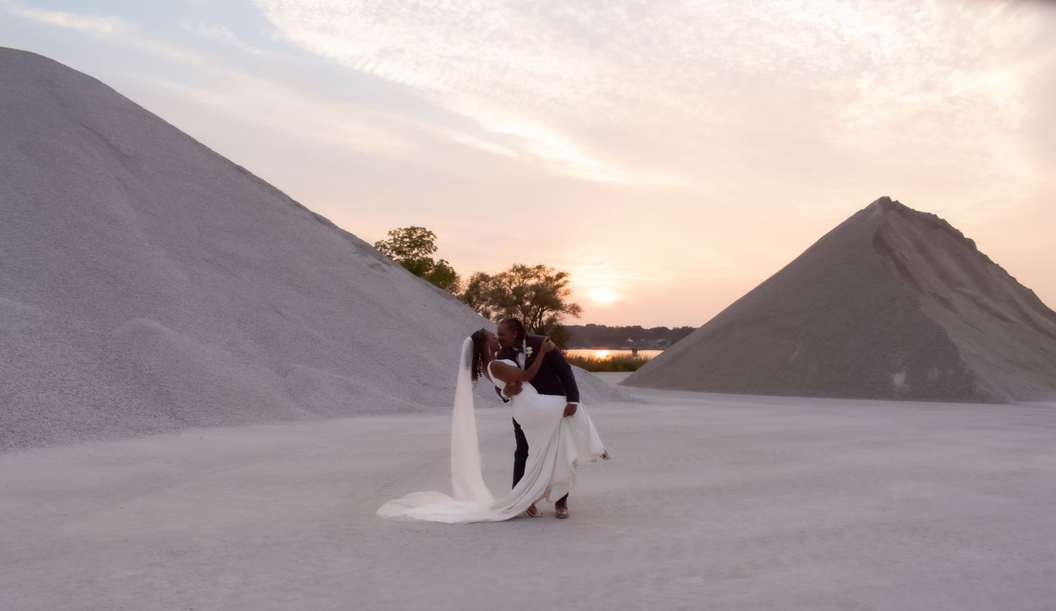A figure in flowing white fabric dances among large salt mounds at sunset creating an ethereal desert scene.