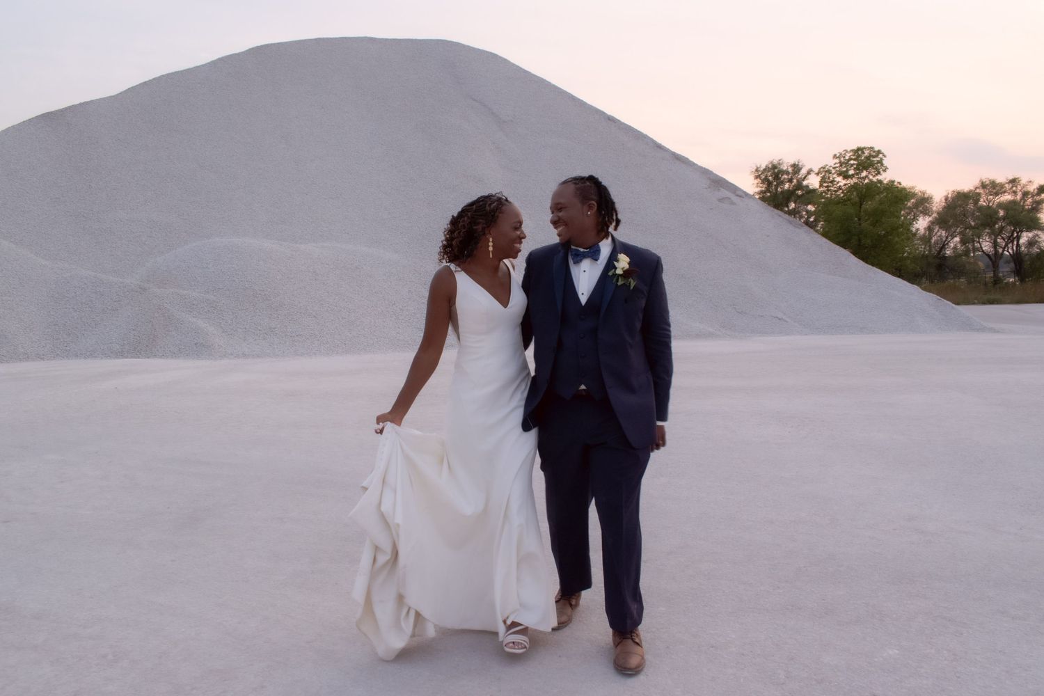A couple walks hand in hand against a striking white sand dune backdrop at dusk.