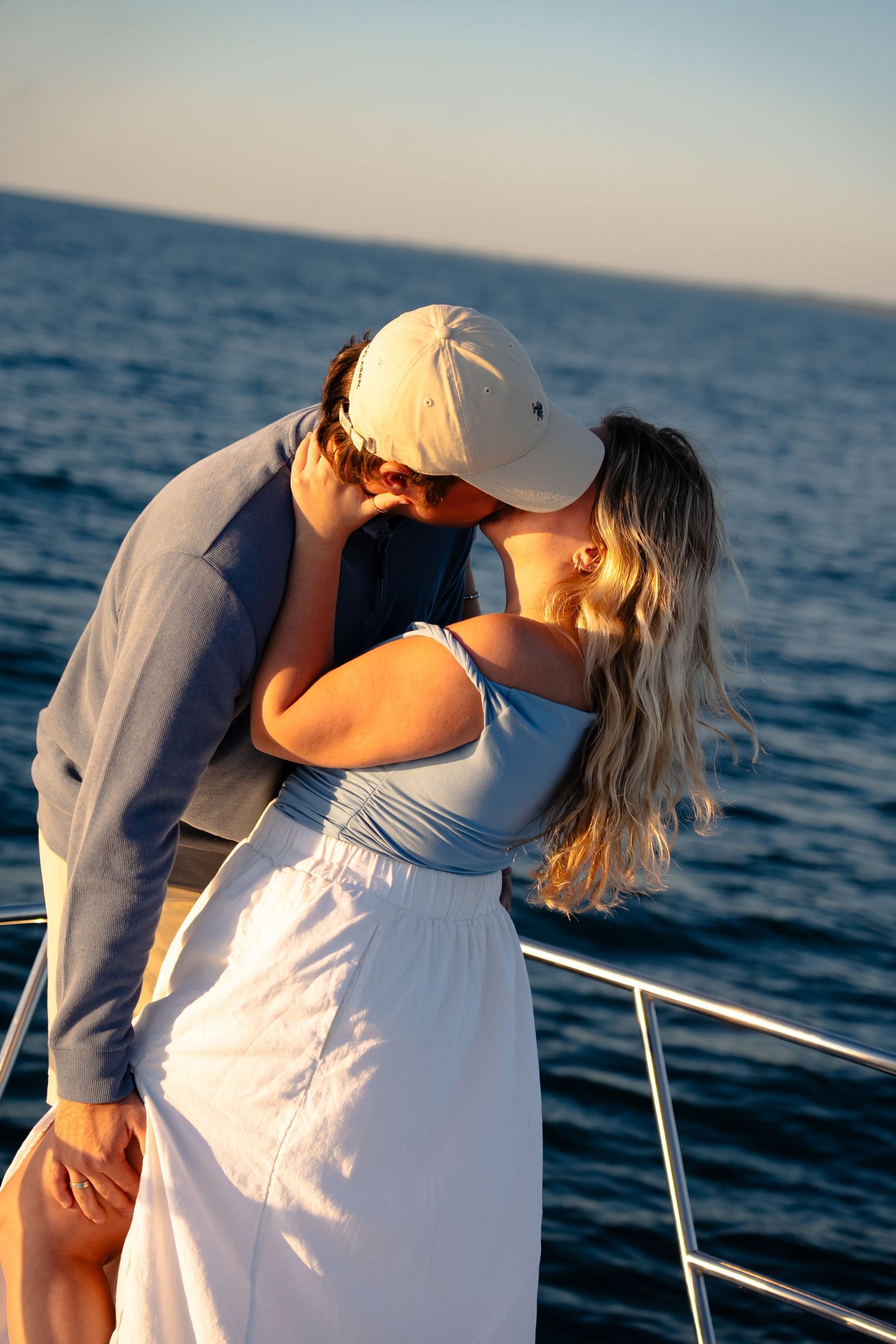 A romantic moment captured at sunset on a boat, showing a couple in a loving embrace against the ocean backdrop.