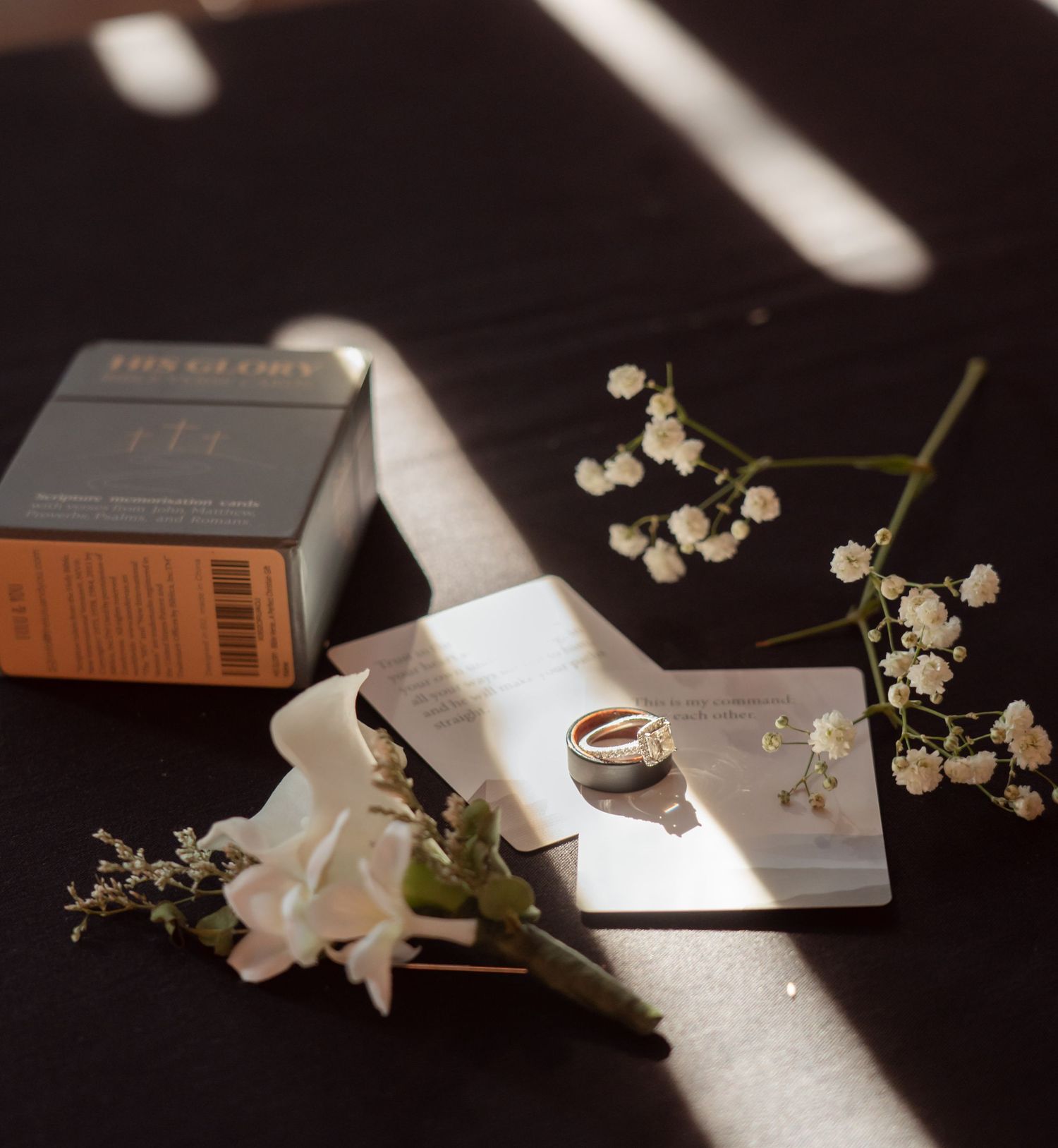 Minimalist still life with a ring, delicate white flowers, and a dark box cast in dramatic natural lighting.