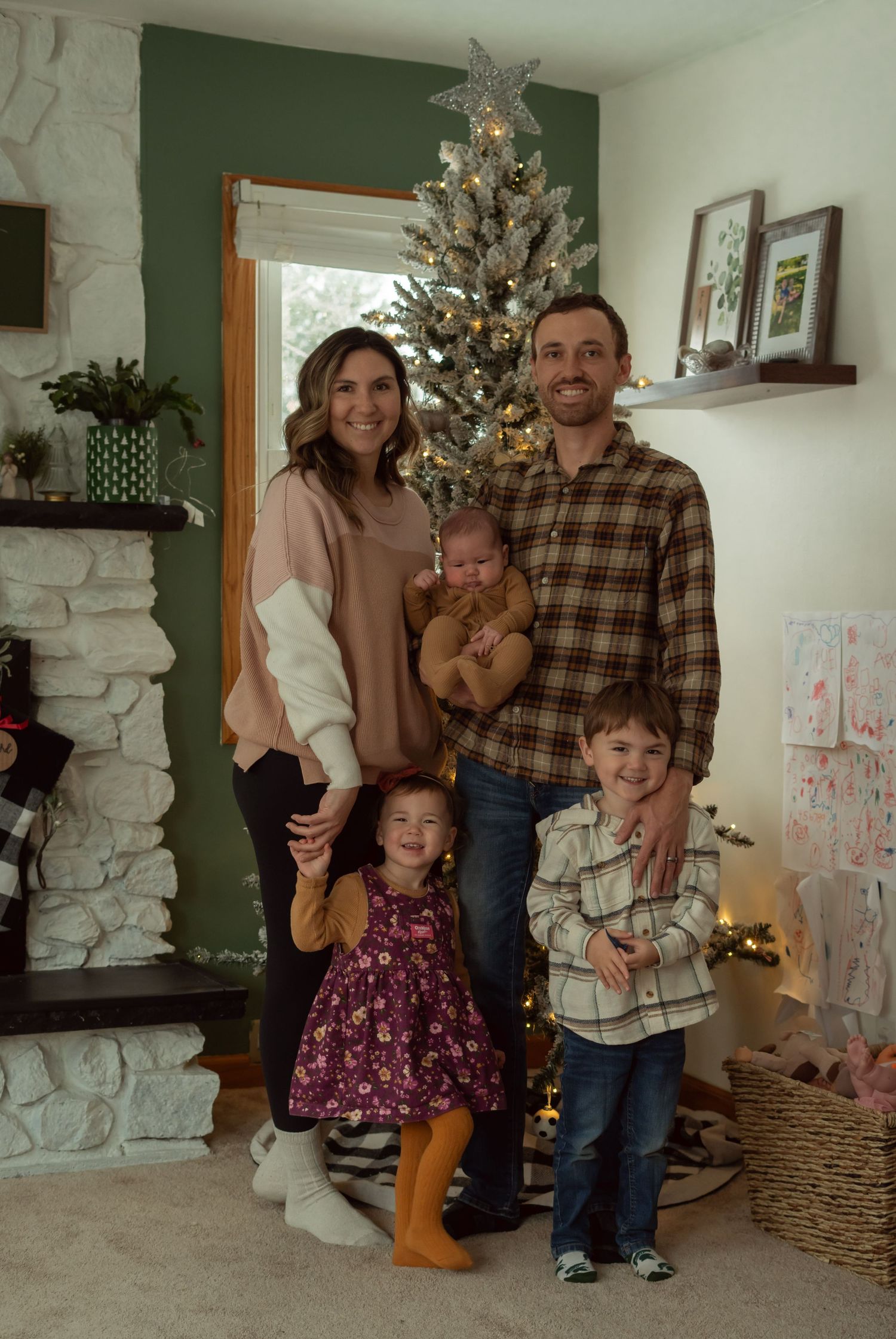 A family poses together in front of their Christmas tree in a cozy living room with white stone fireplace.