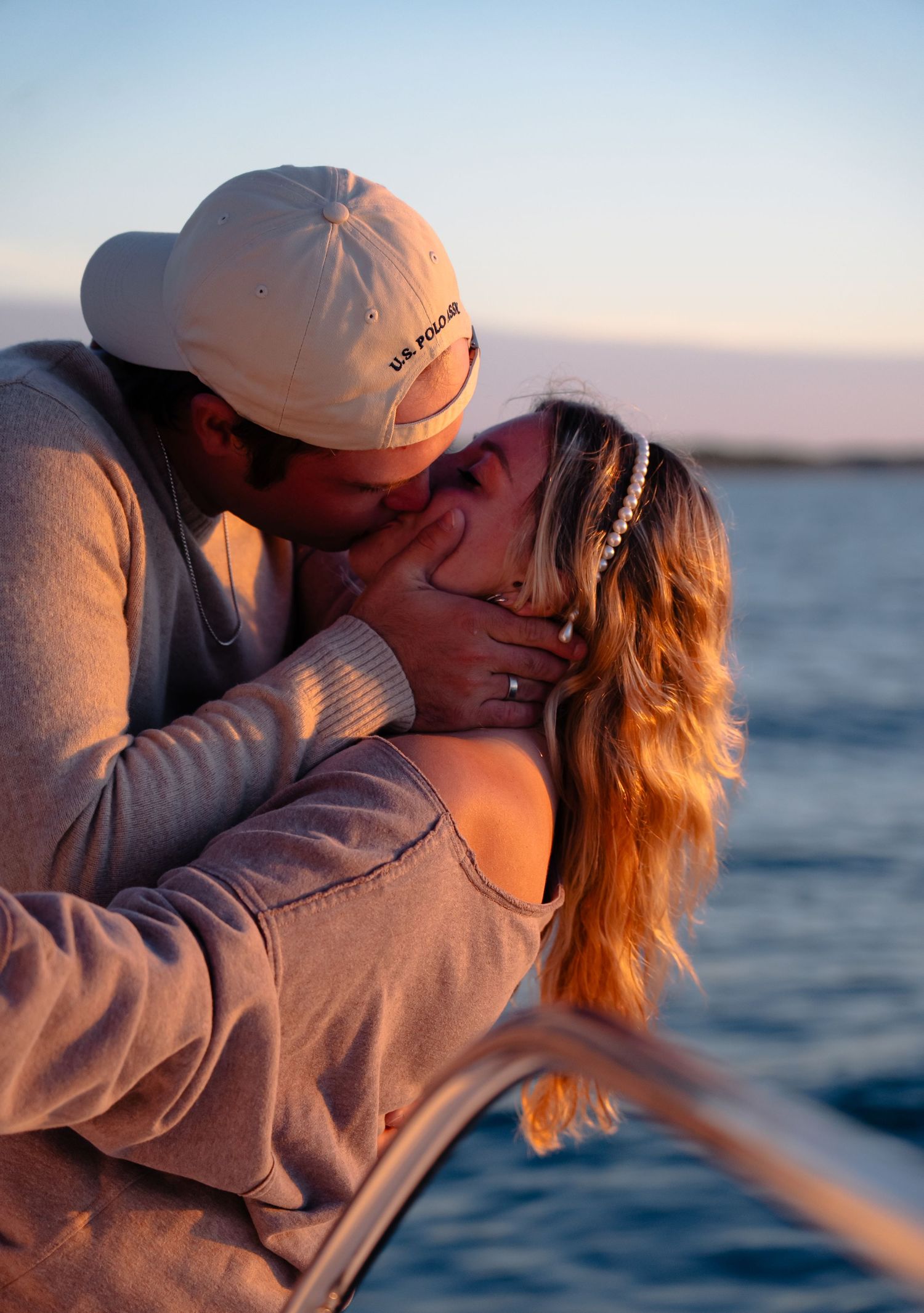 Two people share an intimate kiss while sailing on a boat during golden hour with the ocean in the background.