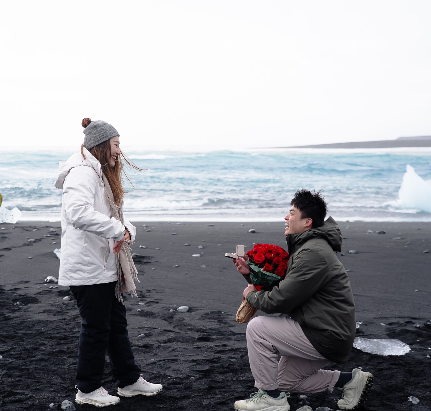 A couple on a black sand beach during a romantic proposal moment by the ocean waves.