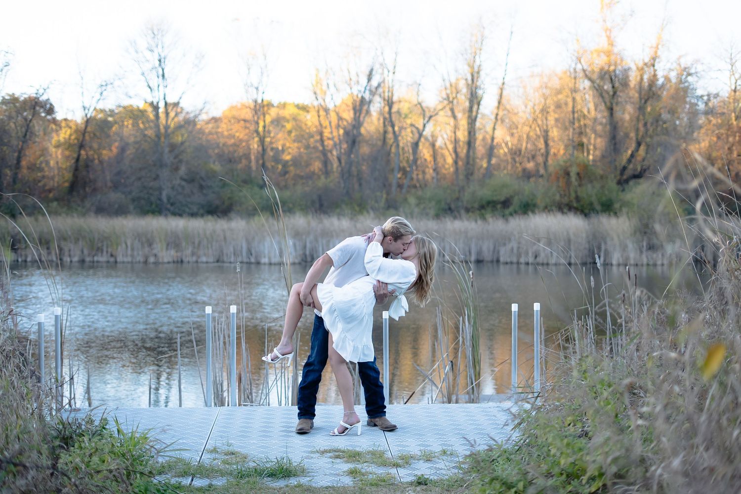 People enjoying a peaceful moment by a tranquil pond surrounded by fall foliage at sunset.