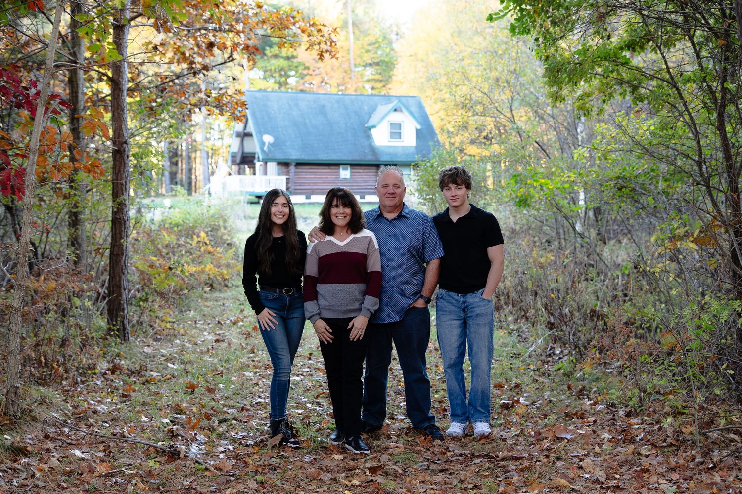 A group of people walking along a wooded autumn trail surrounded by colorful fall foliage.