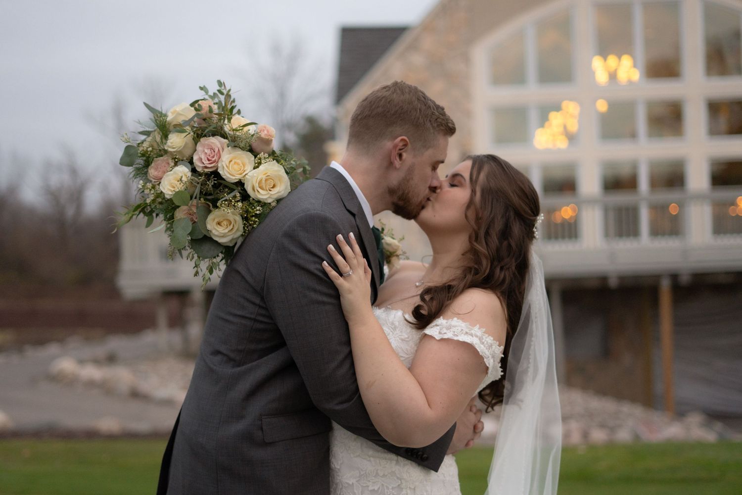 A romantic wedding moment captured outside a modern building at dusk with bouquet.