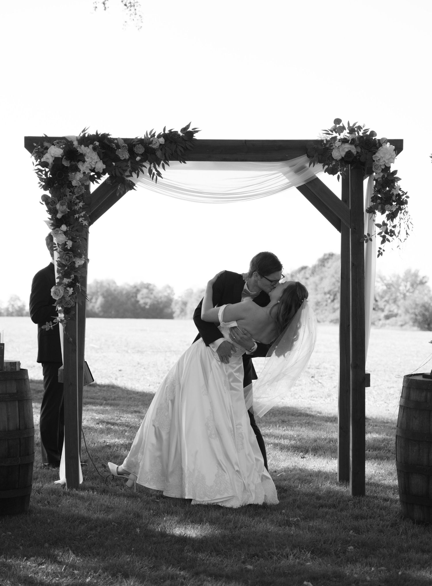 Bride and groom share romantic kiss under decorated wooden arch during outdoor ceremony.