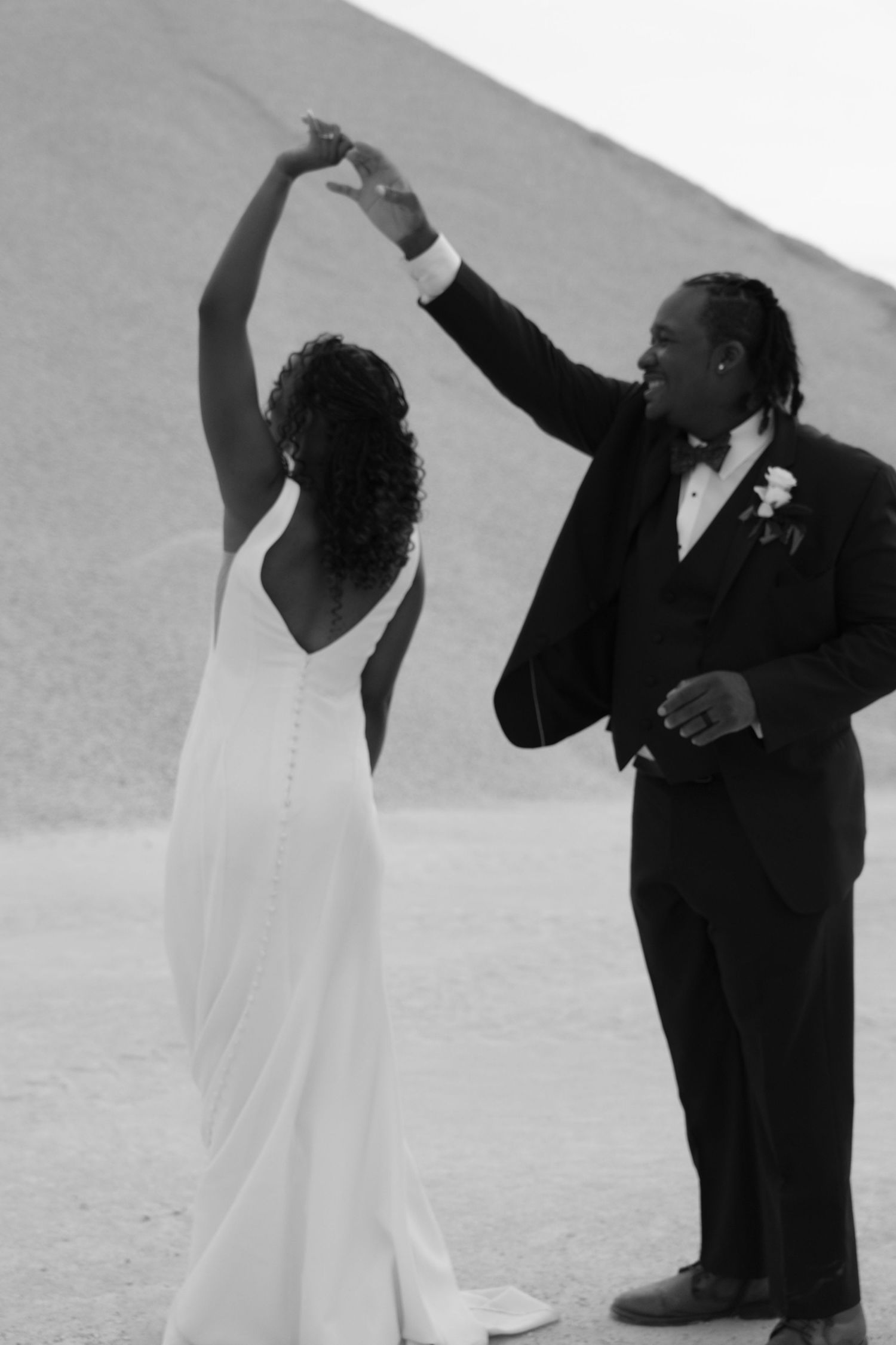 A wedding couple shares a romantic dance moment in black and white against a minimalist outdoor backdrop.