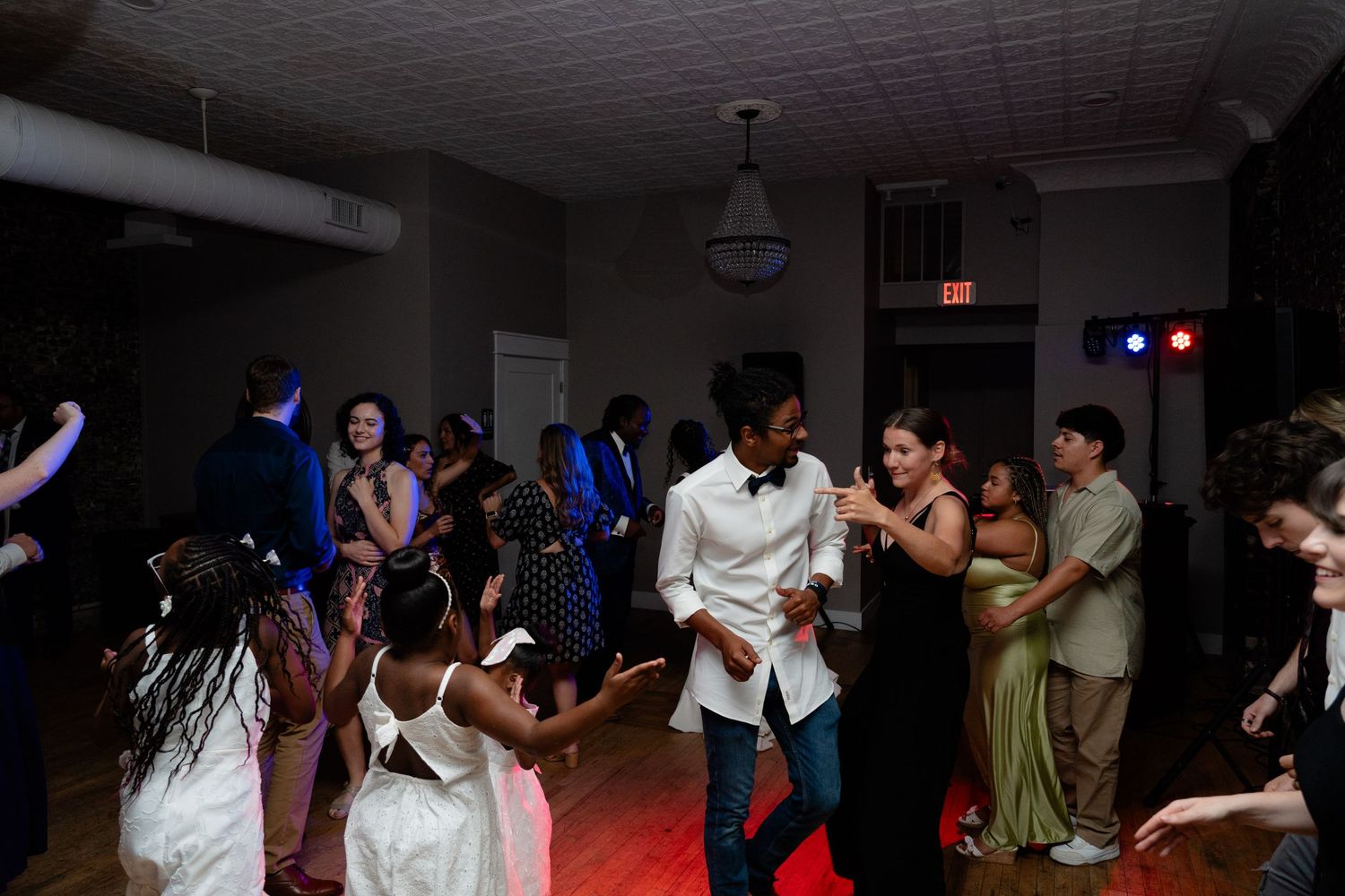 People dancing together at a dimly lit indoor party with colorful lighting effects.