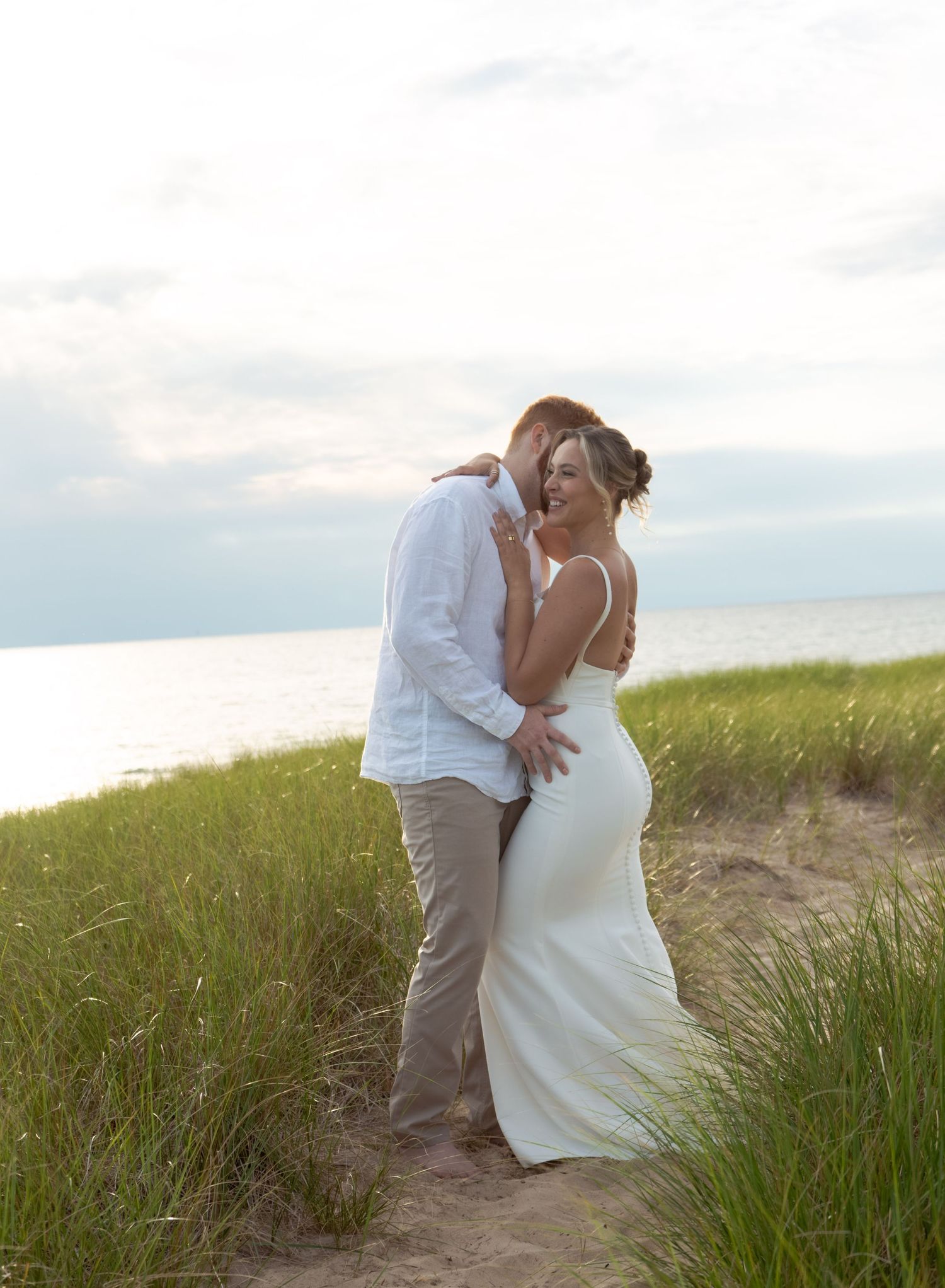 A tender moment between newlyweds embracing on coastal dunes at sunset.
