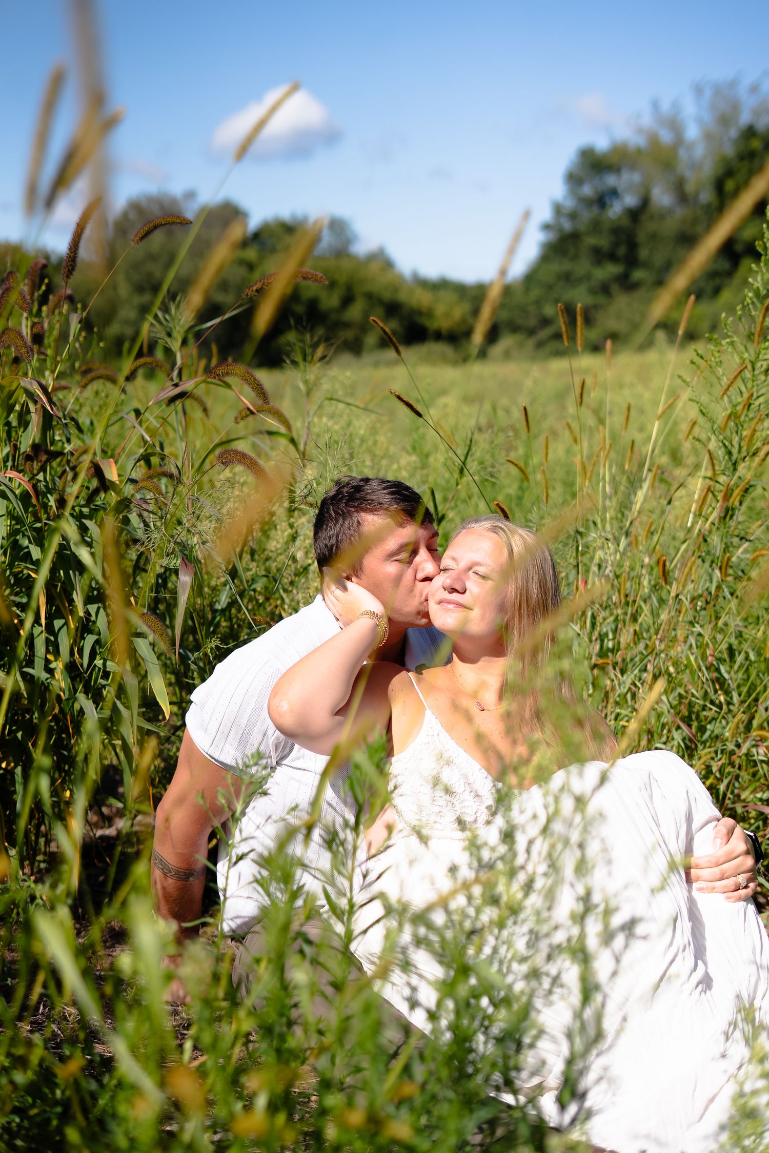 A couple embraces in a field of tall grass on a sunny summer day.