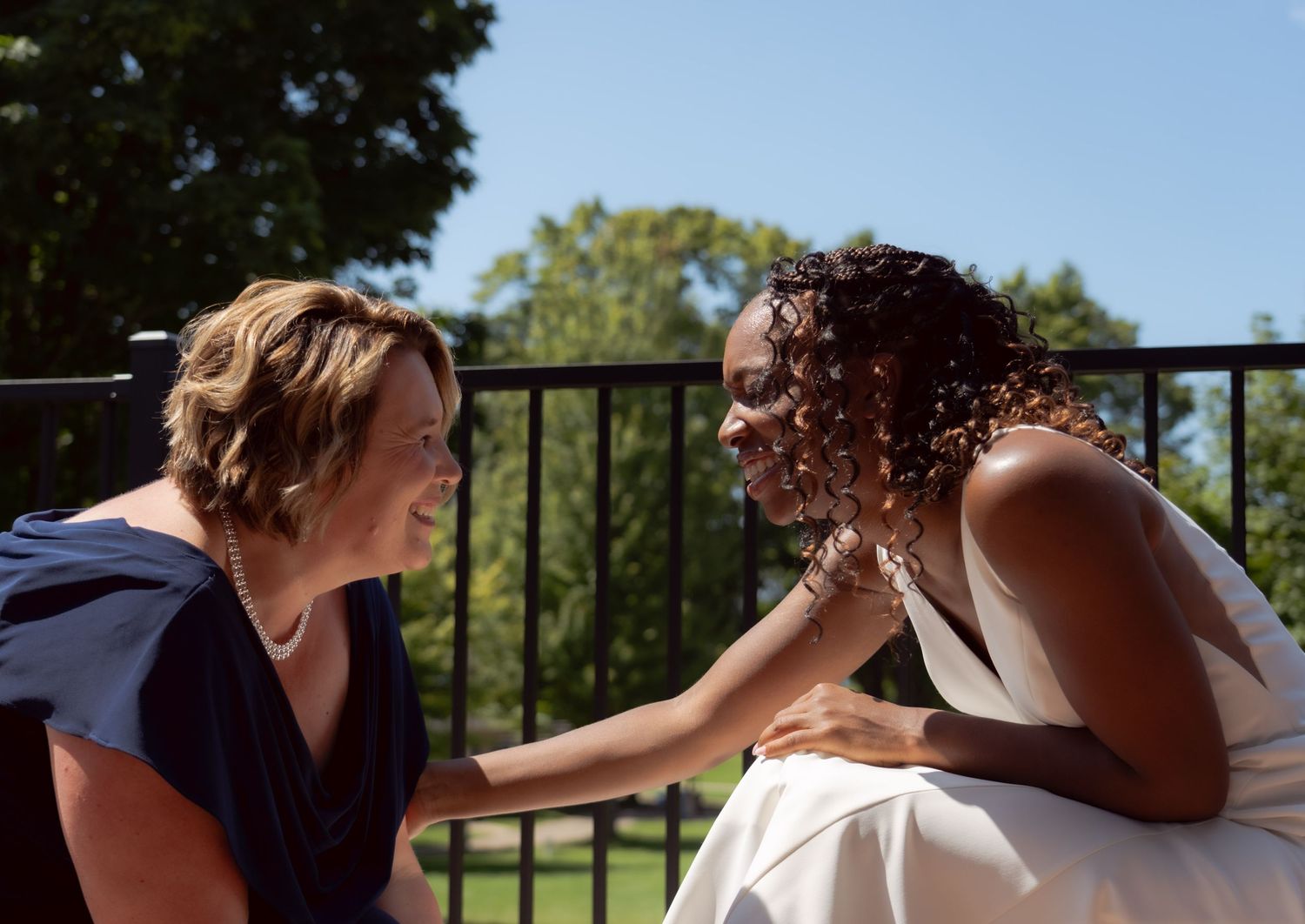 Two people share a joyful moment while sitting outdoors on a balcony with trees visible in the background.