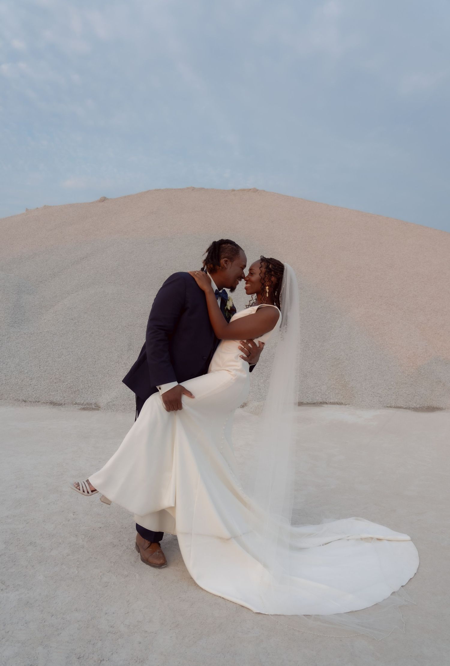 Romantic newlyweds share a tender moment against a desert backdrop during their wedding photoshoot.
