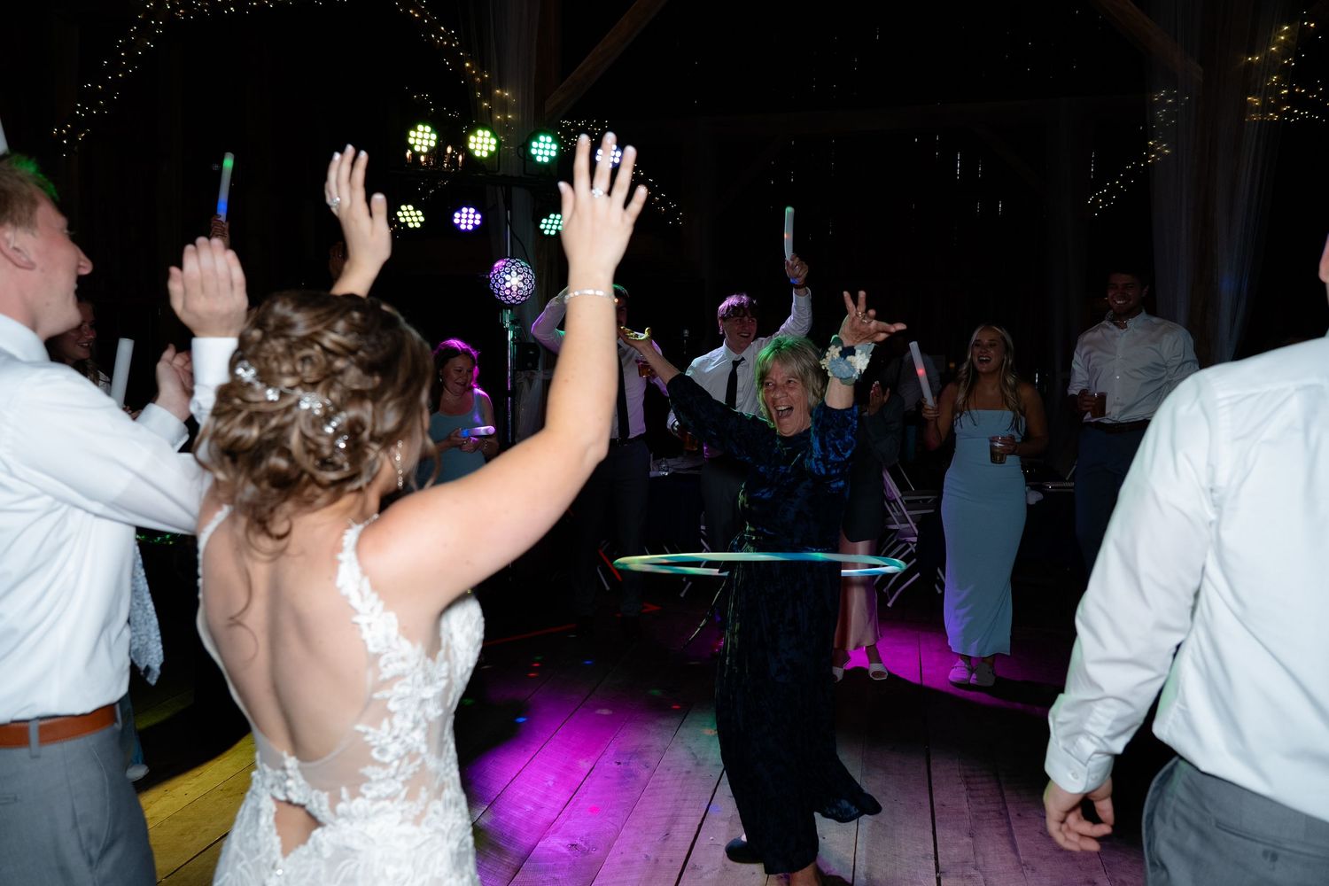 Wedding reception dance party with people raising hands on illuminated dance floor with purple lighting.