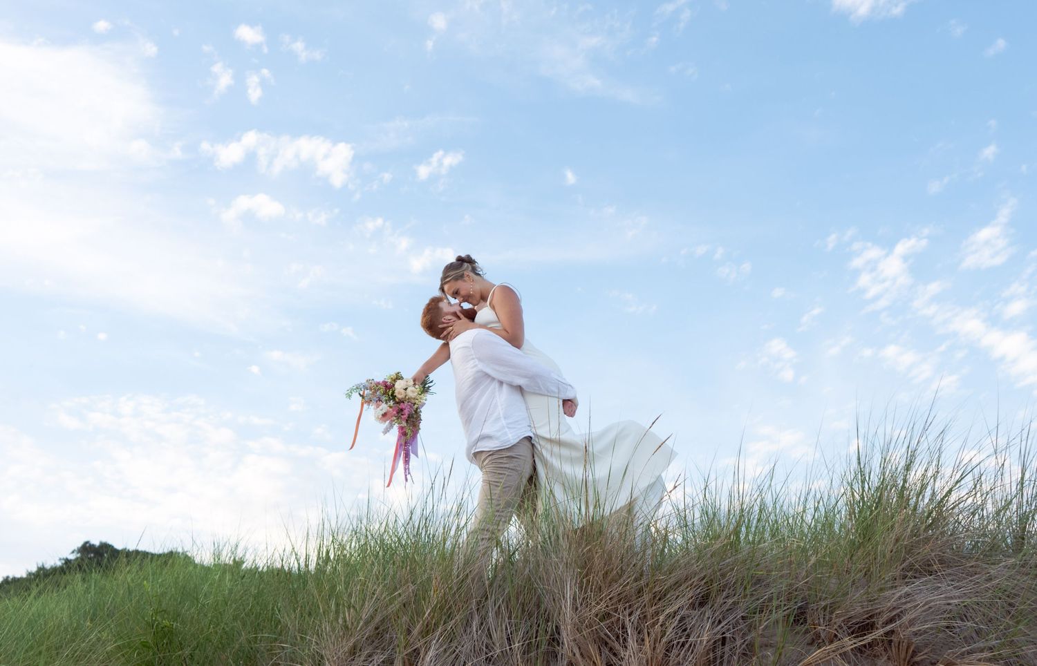 A couple shares an intimate moment on a grassy hill during their wedding.