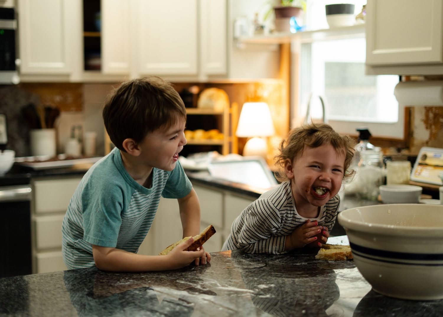 Child lying on countertop licking and tasting ingredients while baking in kitchen.