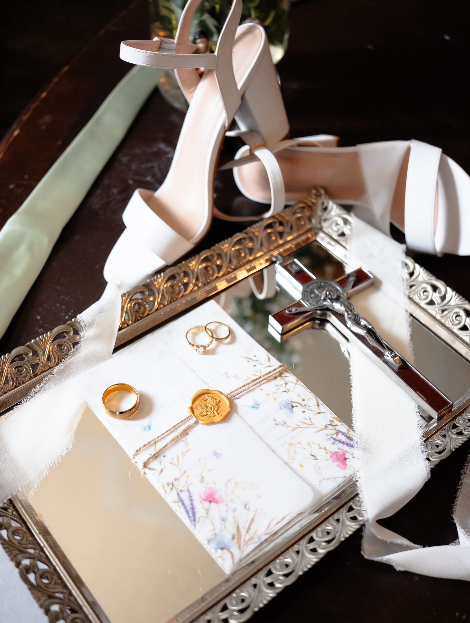 Wedding accessories including white shoes, gold rings, and decorative key arranged on an ornate silver tray with white ribbon.