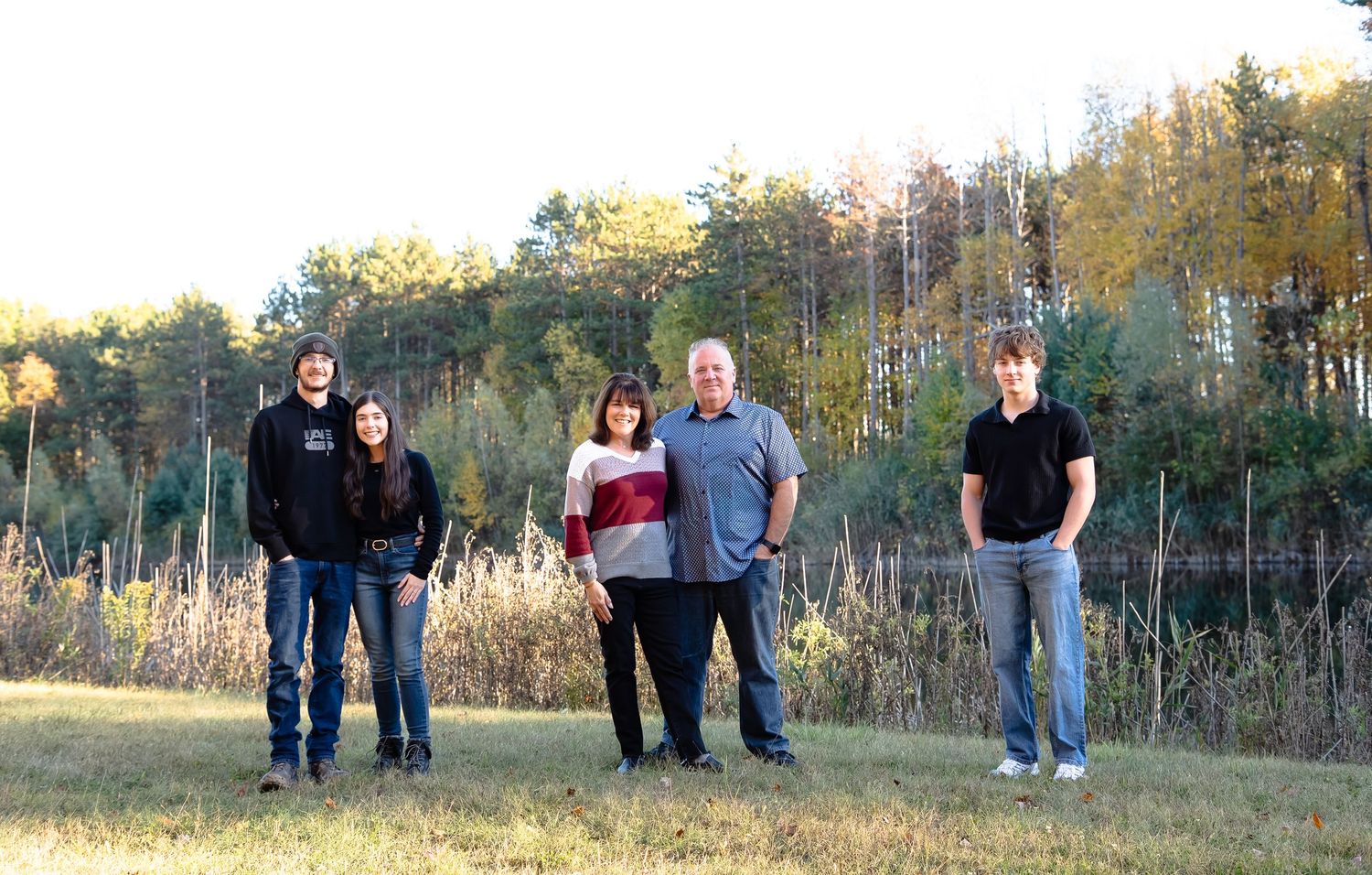 Family group poses together outdoors in autumn with trees and natural scenery in the background.