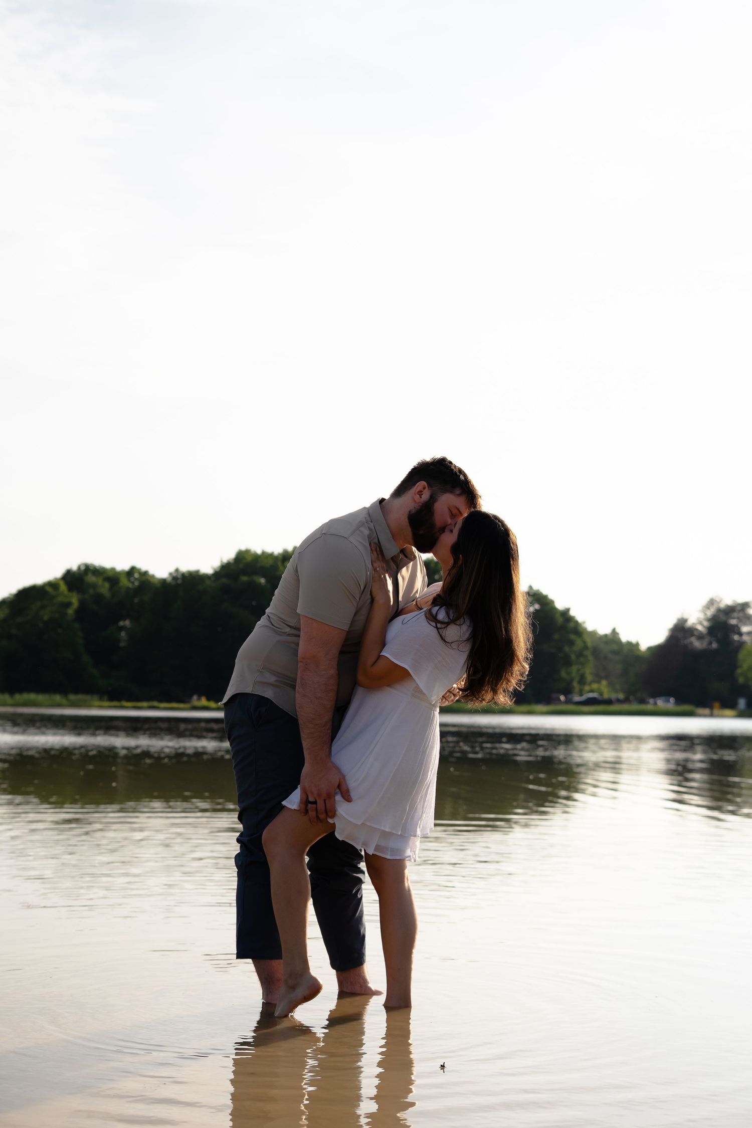 A couple stands at the edge of a serene lake during sunset, creating a romantic silhouette against the water.