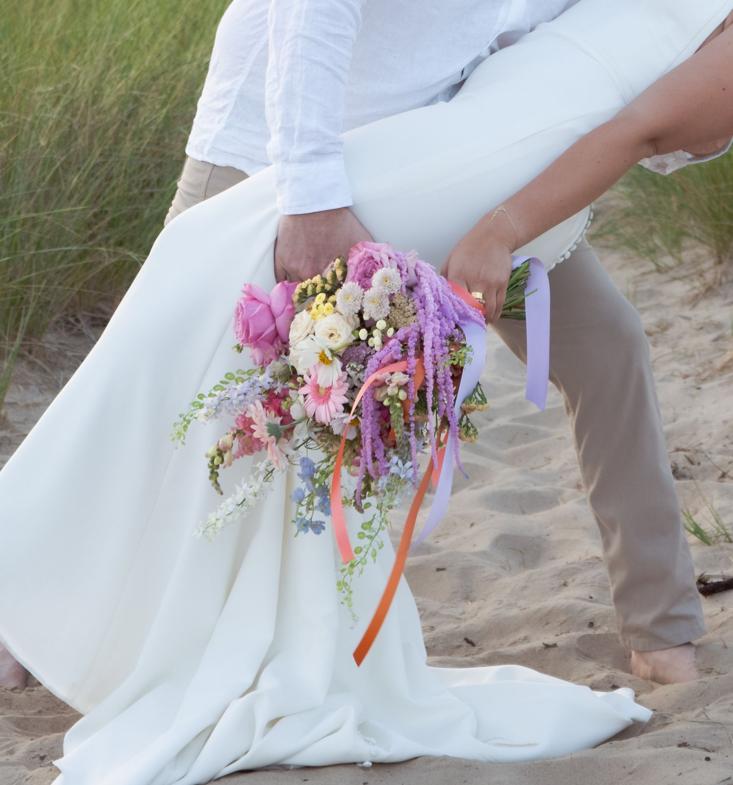 A colorful bridal bouquet with pink and purple flowers held against a white dress.