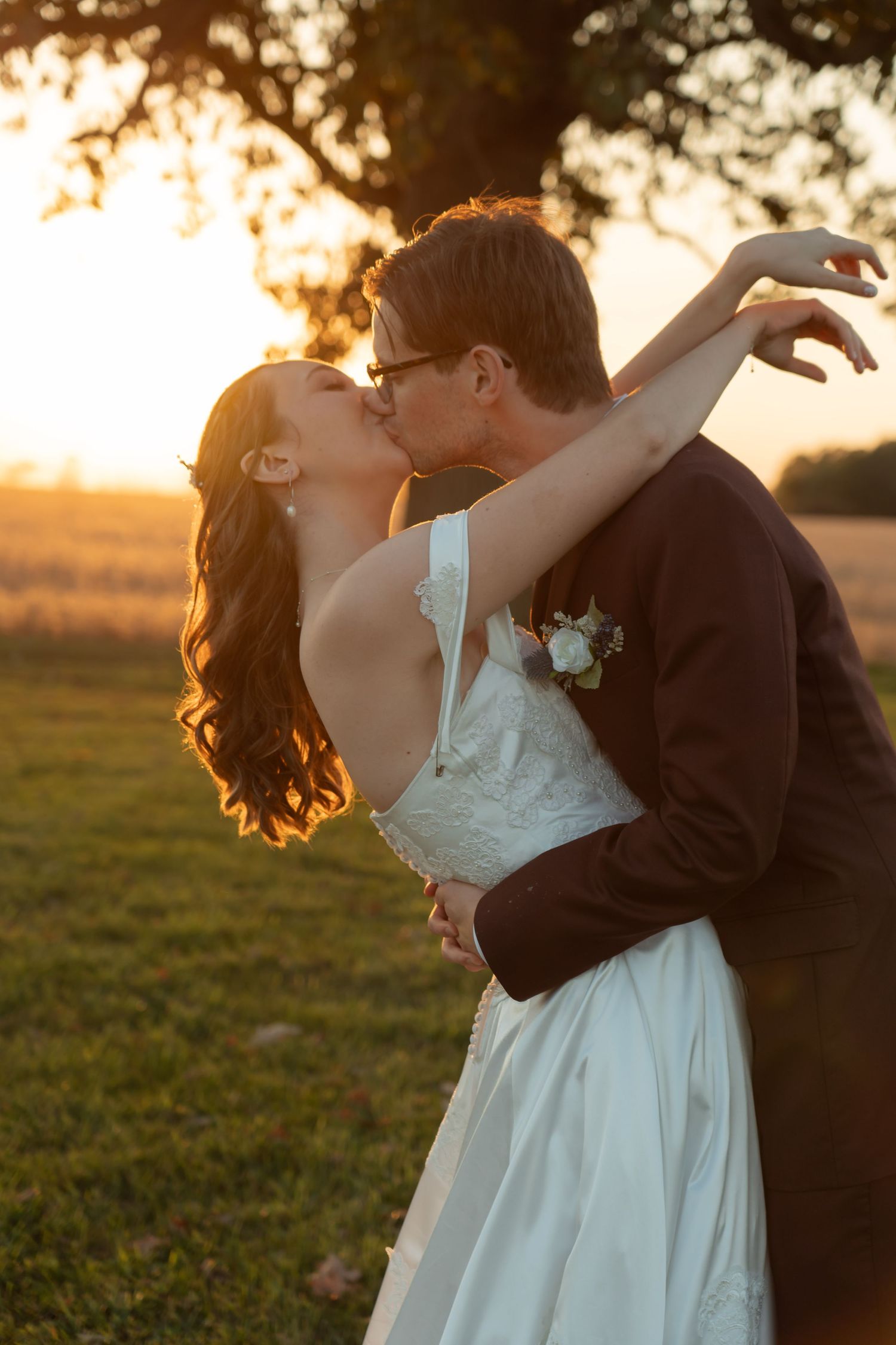 A romantic sunset kiss between a couple on their wedding day with a warm golden glow in the background.